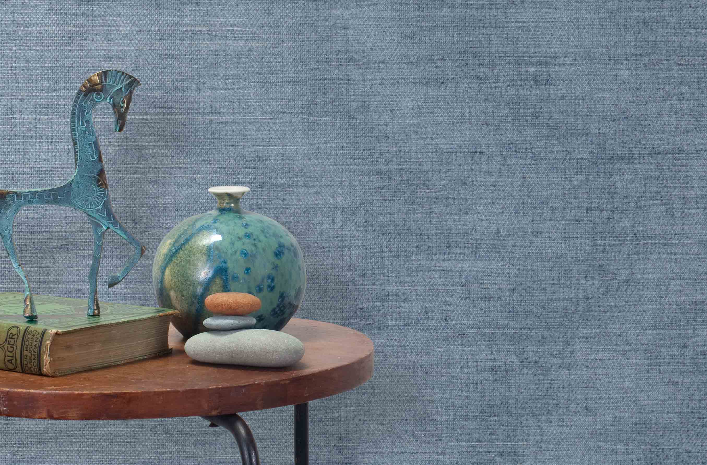 End table with a vase, horse sculpture and stones in front of a wall covered in sisal grasscloth in mottled blue.