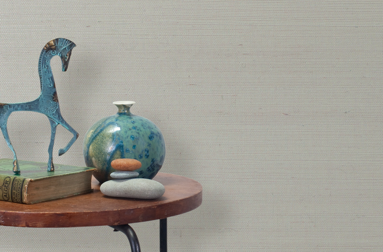 End table with a vase, horse sculpture and stones in front of a wall covered in sisal grasscloth in mottled gray.
