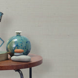 End table with a vase, horse sculpture and stones in front of a wall covered in sisal grasscloth in mottled gray.