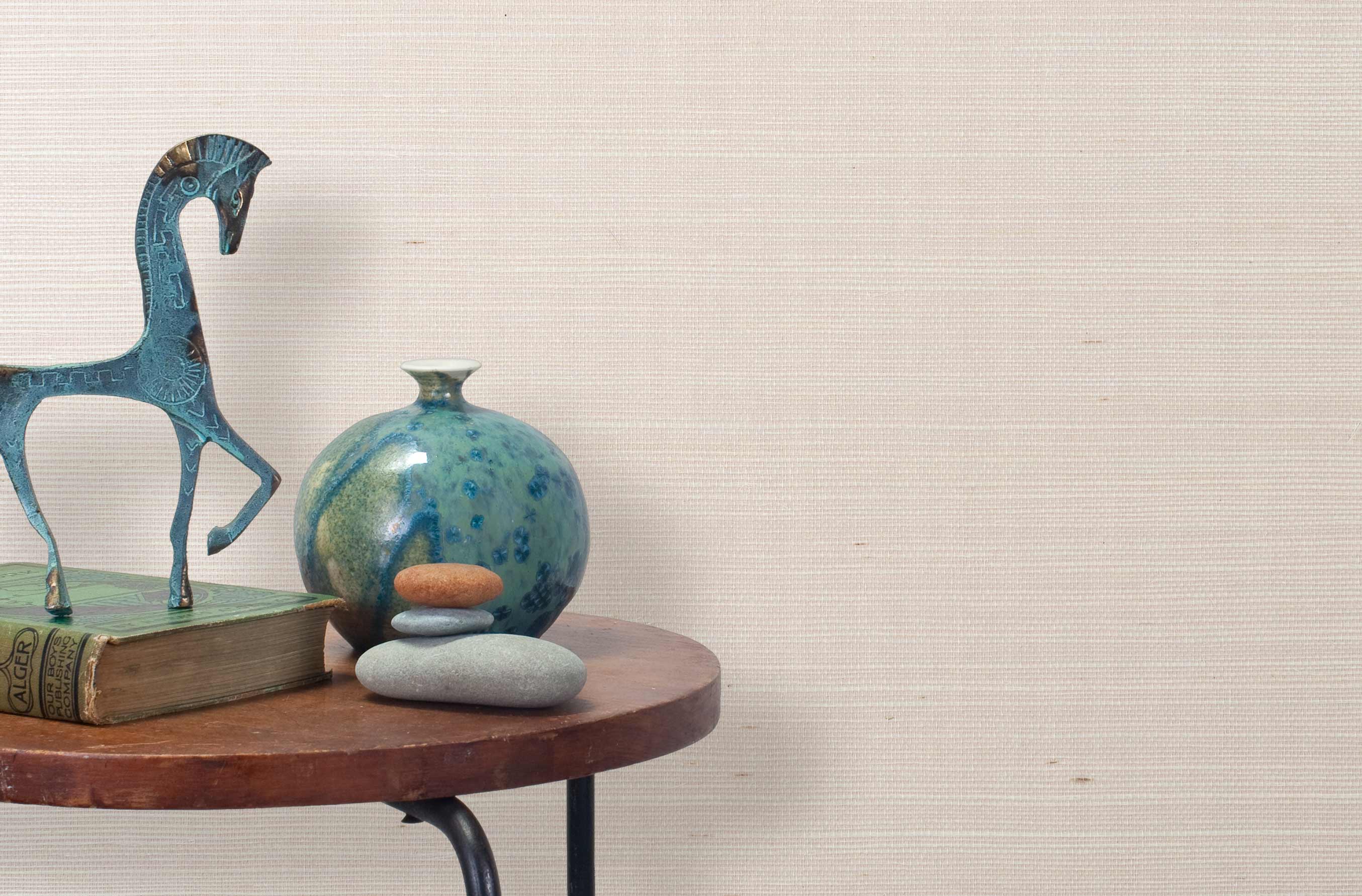 End table with a vase, horse sculpture and stones in front of a wall covered in sisal grasscloth in mottled pink.