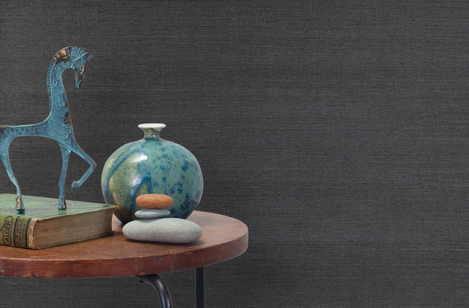 End table with a vase, horse sculpture and stones in front of a wall covered in sisal grasscloth in mottled charcoal.