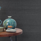 End table with a vase, horse sculpture and stones in front of a wall covered in sisal grasscloth in mottled charcoal.