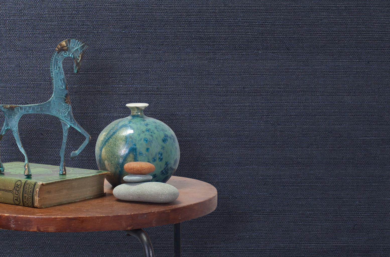 End table with a vase, horse sculpture and stones in front of a wall covered in sisal grasscloth in mottled navy.