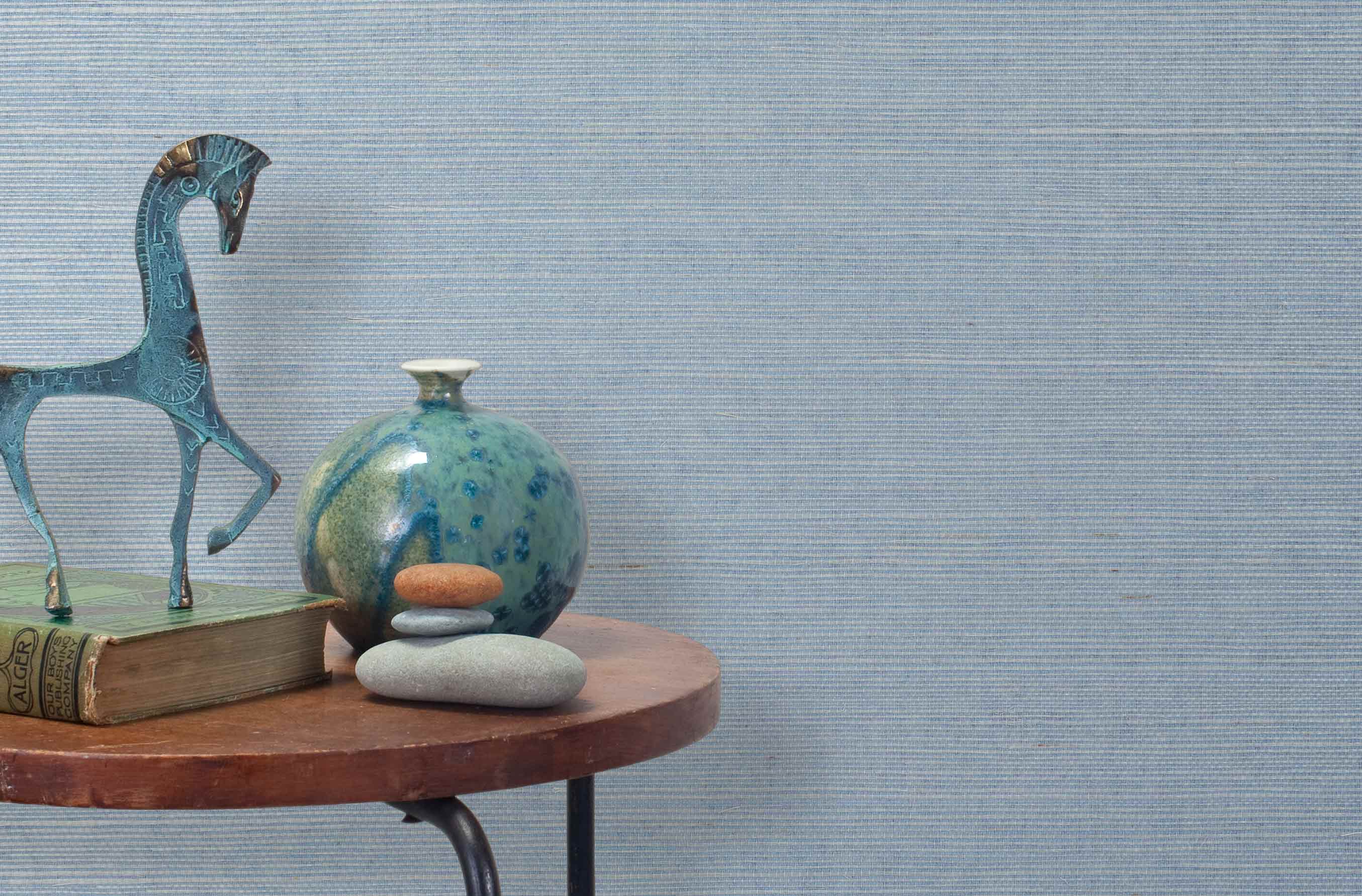 End table with a vase, horse sculpture and stones in front of a wall covered in sisal grasscloth in light gray and blue.