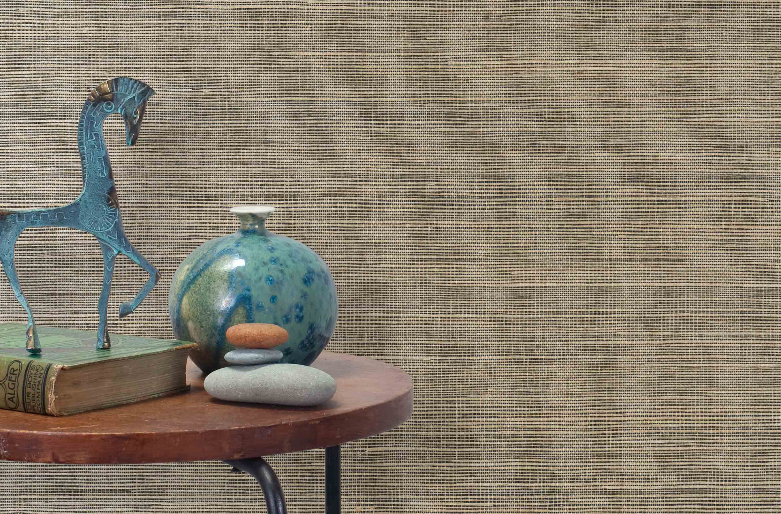 End table with a vase, horse sculpture and stones in front of a wall covered in sisal grasscloth in mottled tan and black.