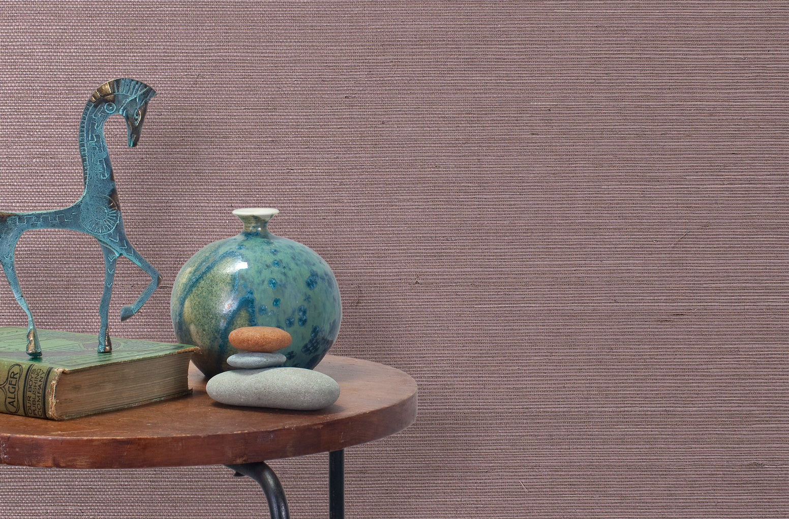 End table with a vase, horse sculpture and stones in front of a wall covered in sisal grasscloth in mottled mauve.