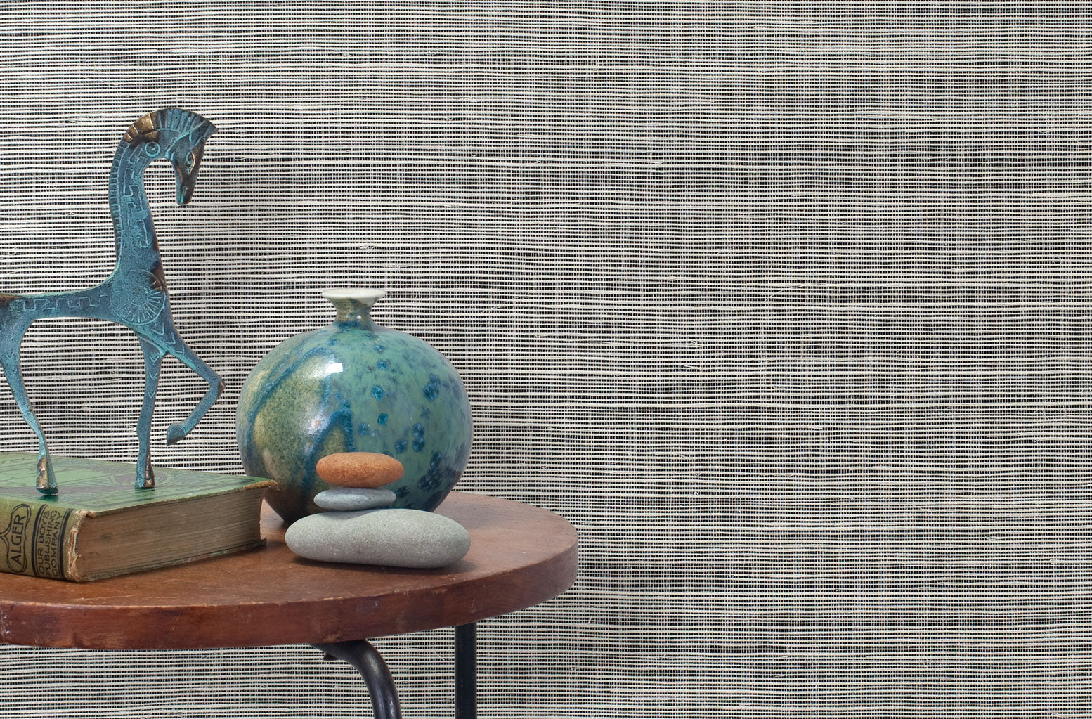 End table with a vase, horse sculpture and stones in front of a wall covered in sisal grasscloth in mottled black and white.