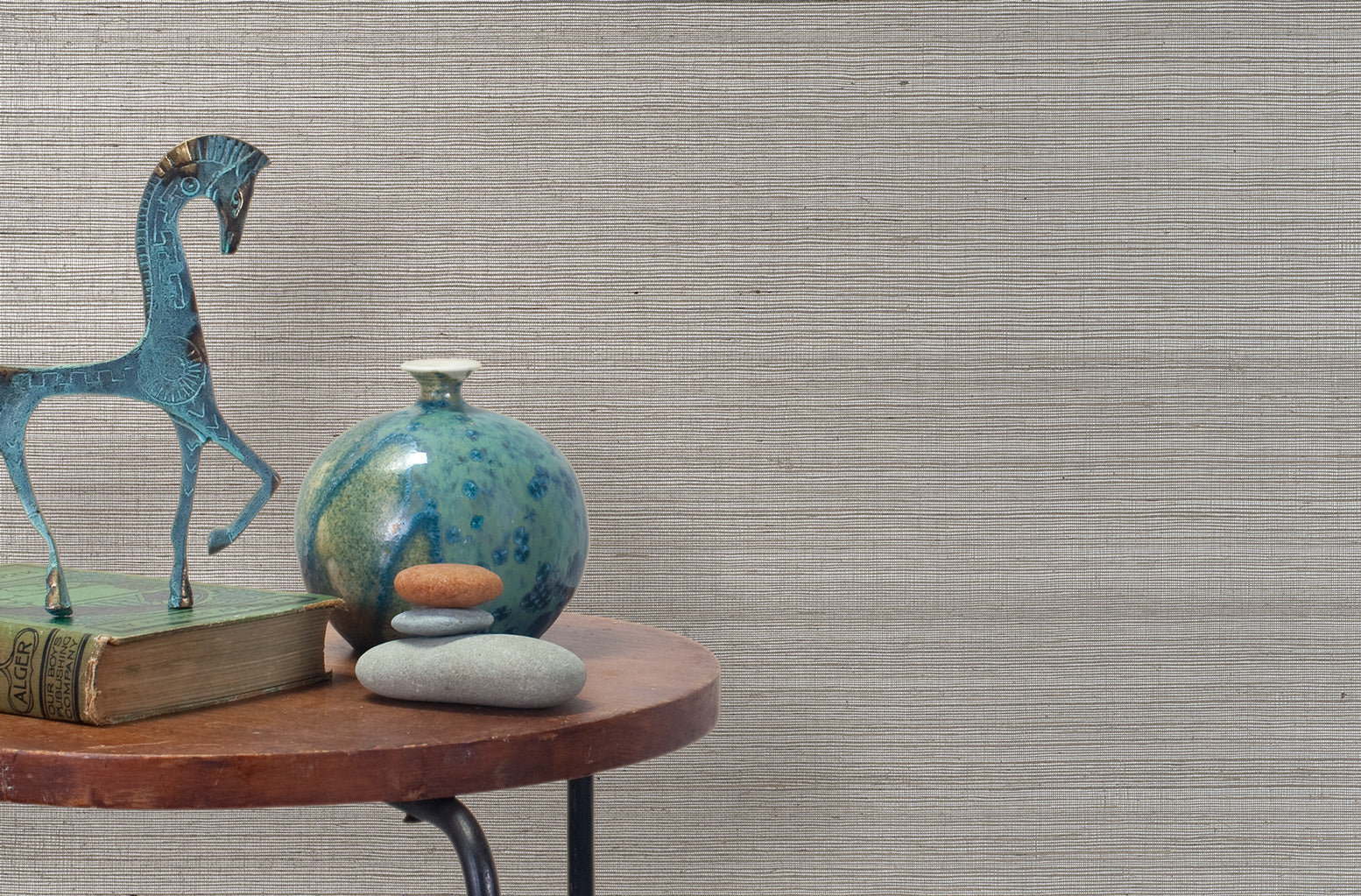 End table with a vase, horse sculpture and stones in front of a wall covered in sisal grasscloth in mottled gray.