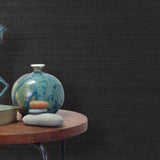 End table with a vase, horse sculpture and stones in front of a wall covered in sisal grasscloth in black.