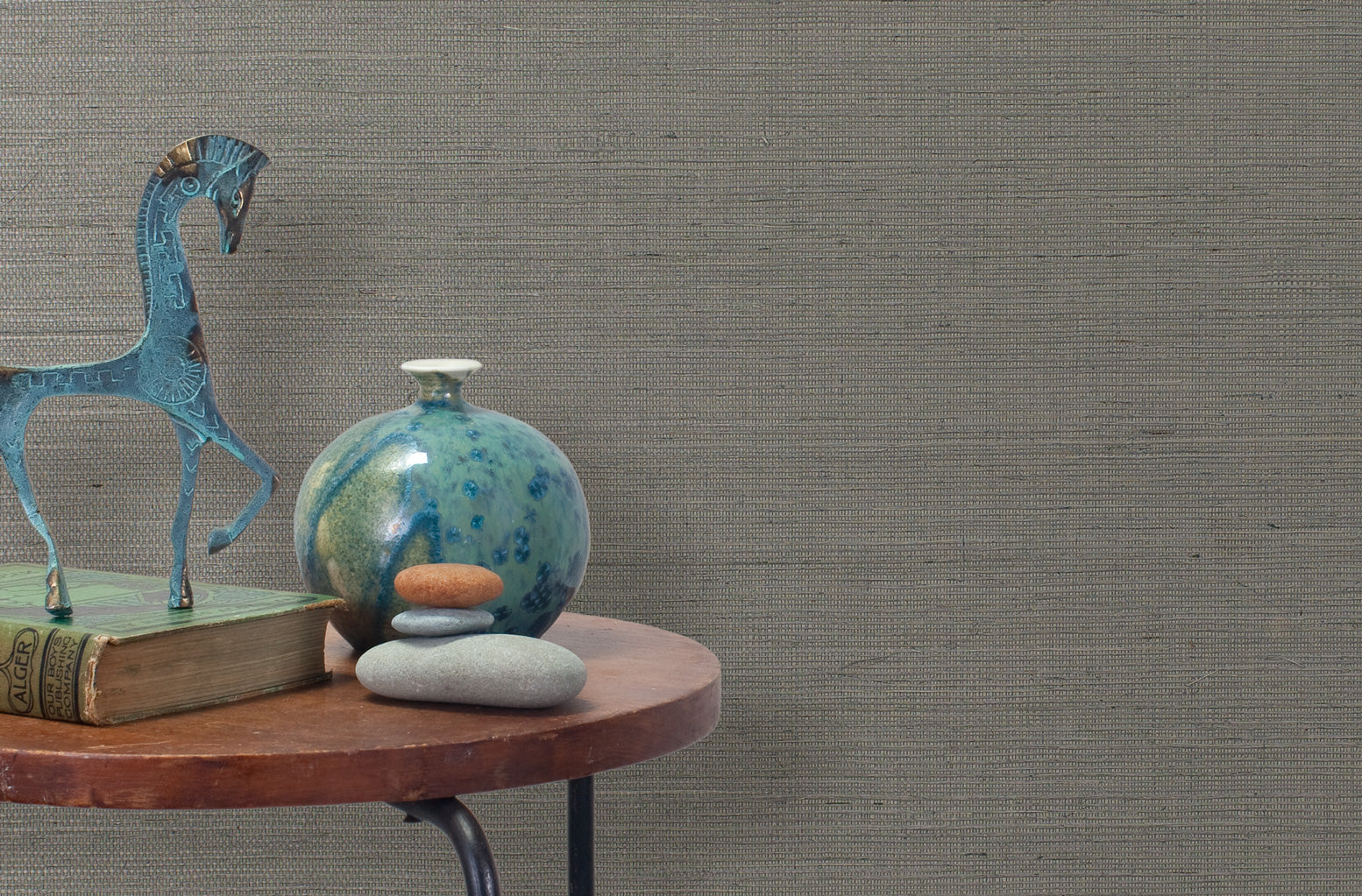 End table with a vase, horse sculpture and stones in front of a wall covered in sisal grasscloth in mottled gray.