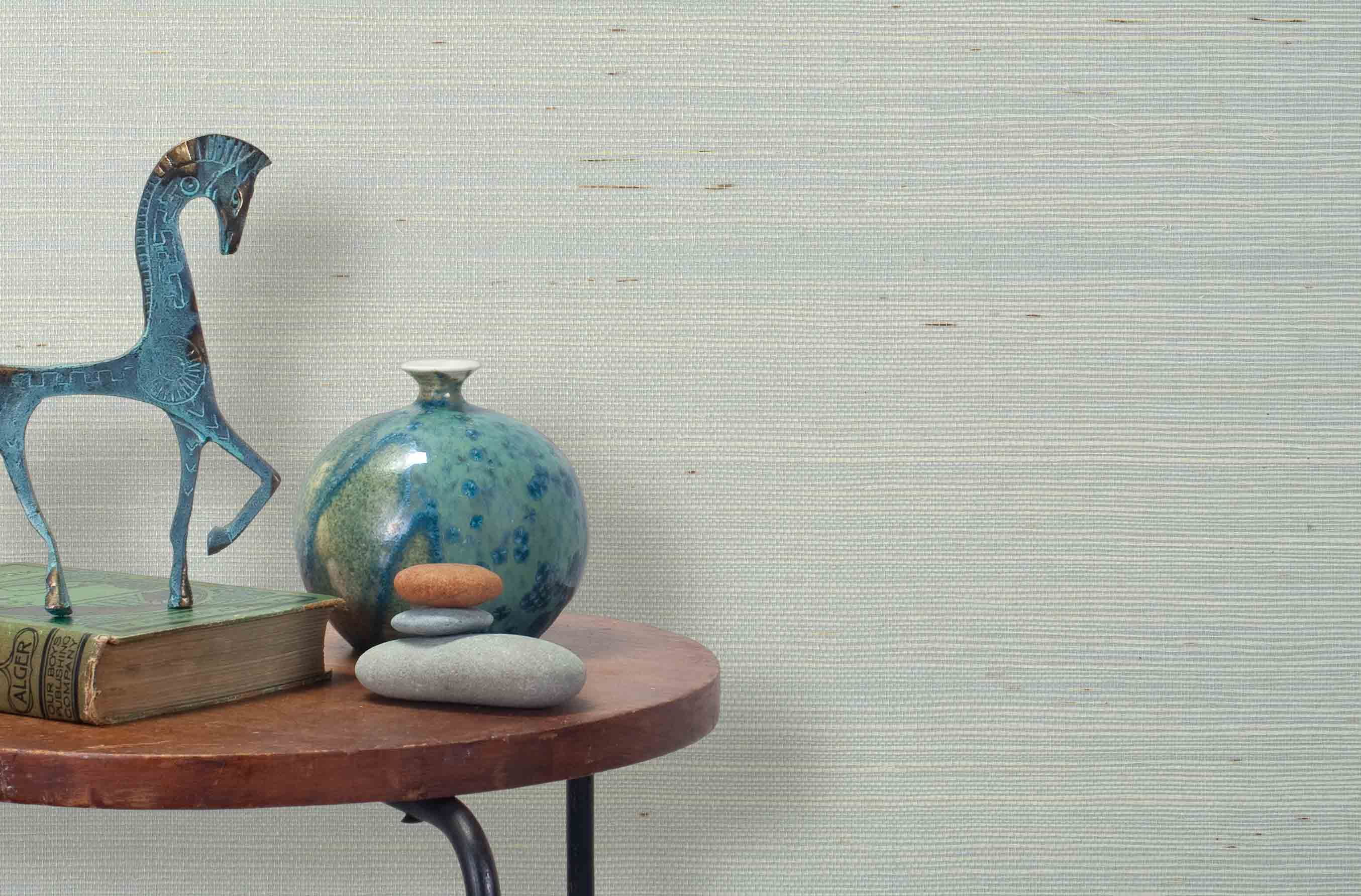 End table with a vase, horse sculpture and stones in front of a wall covered in sisal grasscloth in mottled pale blue.