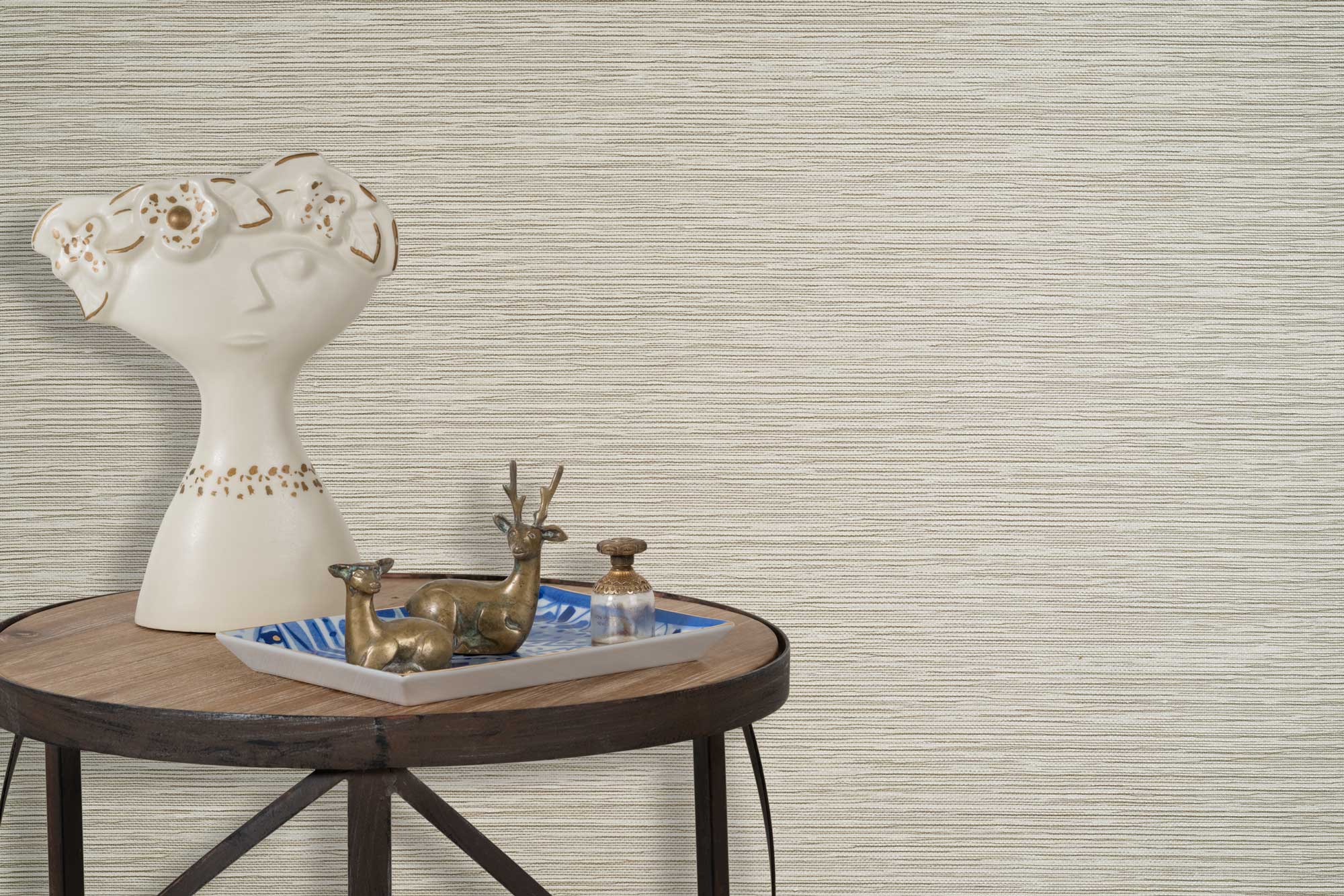 End table with a tray and some sculptures in front of a wall papered in textured grasscloth in cream. 