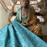 Sculpture of Buddha against antique mirror with draped blue greek key fabric.