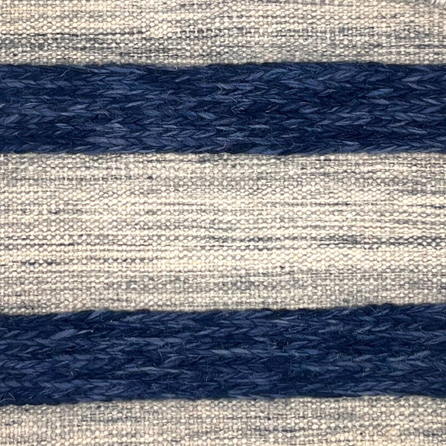 A flatweave rug with stripes of grey and ivory alternating with raised woven strips in shades of dark blue.