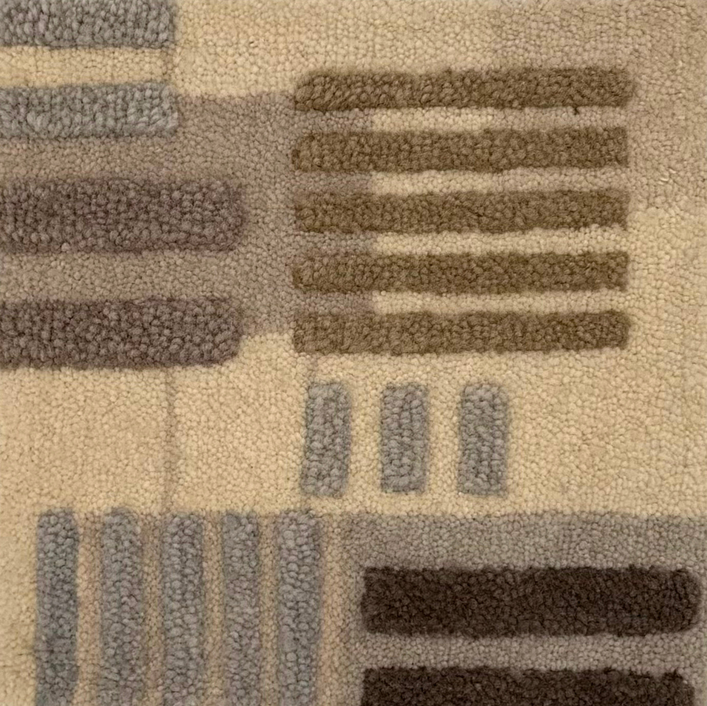 Close-up of a handknotted rug with a raised geometric pattern in beige, taupe, gray, and dark brown.