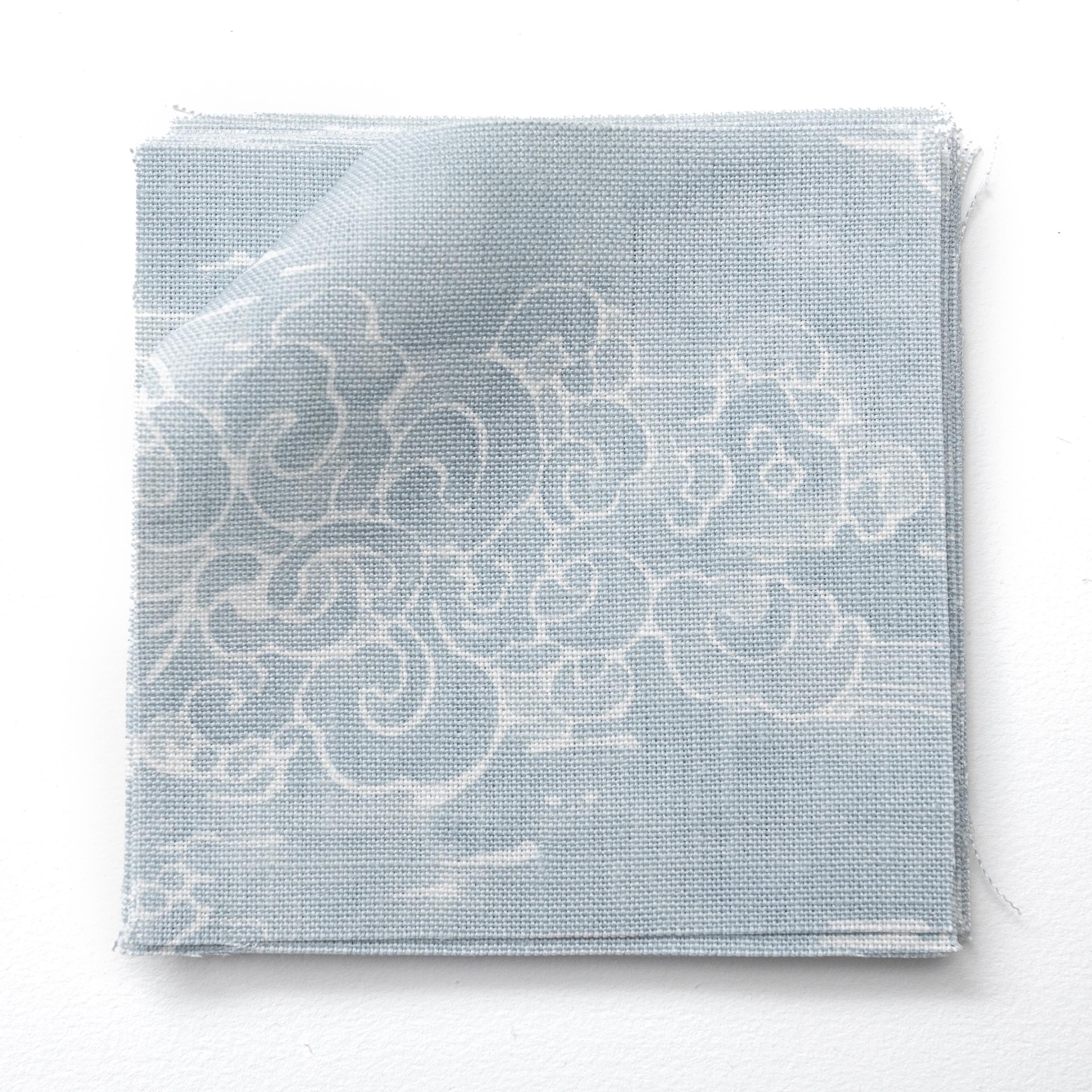 Fabric swatches in a painterly cloud pattern in white on a pastel blue watercolor field.