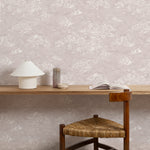 A wooden chair stands in wooden desk front of a wall papered in a painterly cloud pattern in white on a pastel purple field.