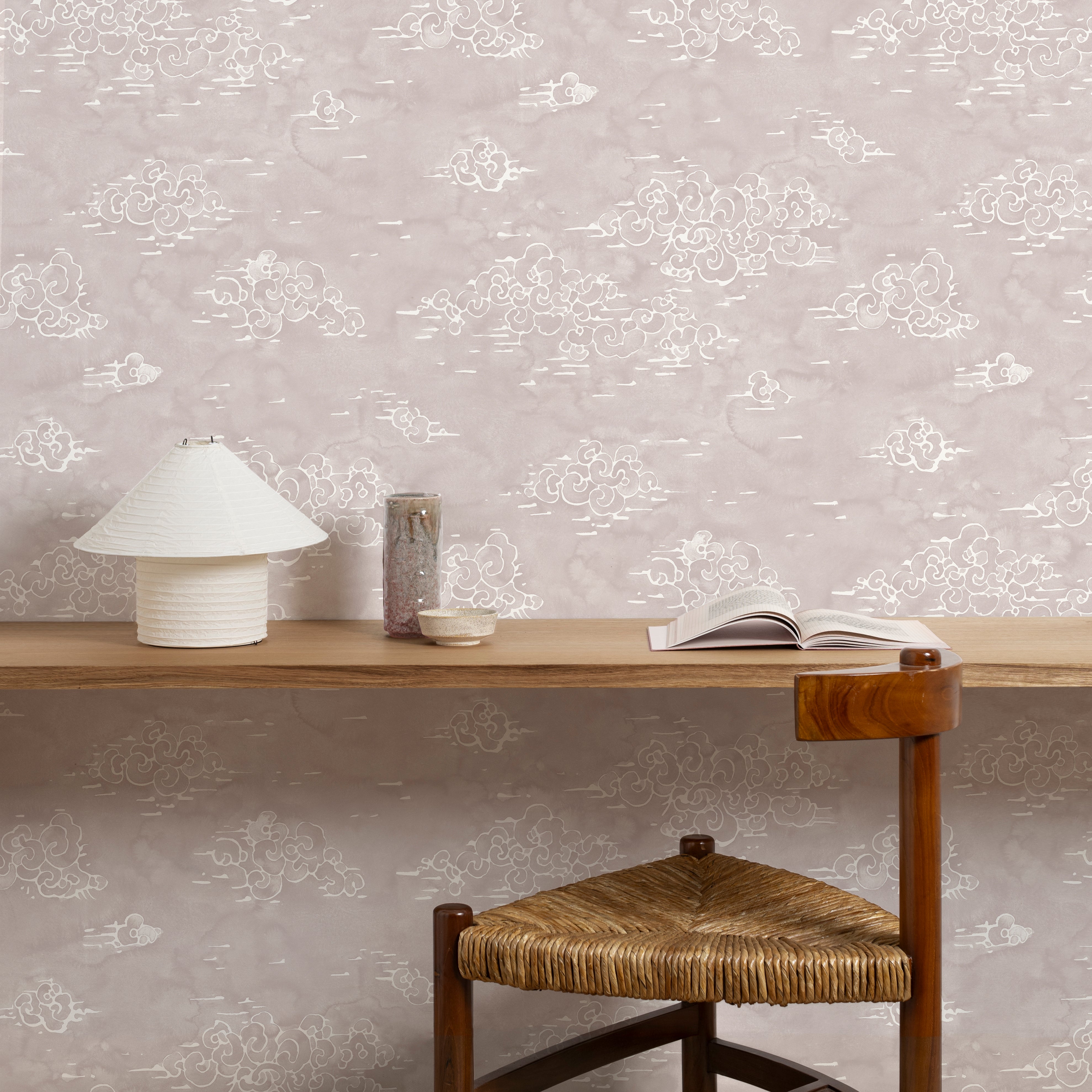 A wooden chair stands in wooden desk front of a wall papered in a painterly cloud pattern in white on a pastel purple field.