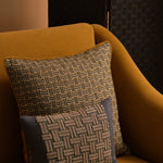 Ochre yellow couch with two embroidered throw pillows in a basketweave design in shades of green, ecru and navy. 