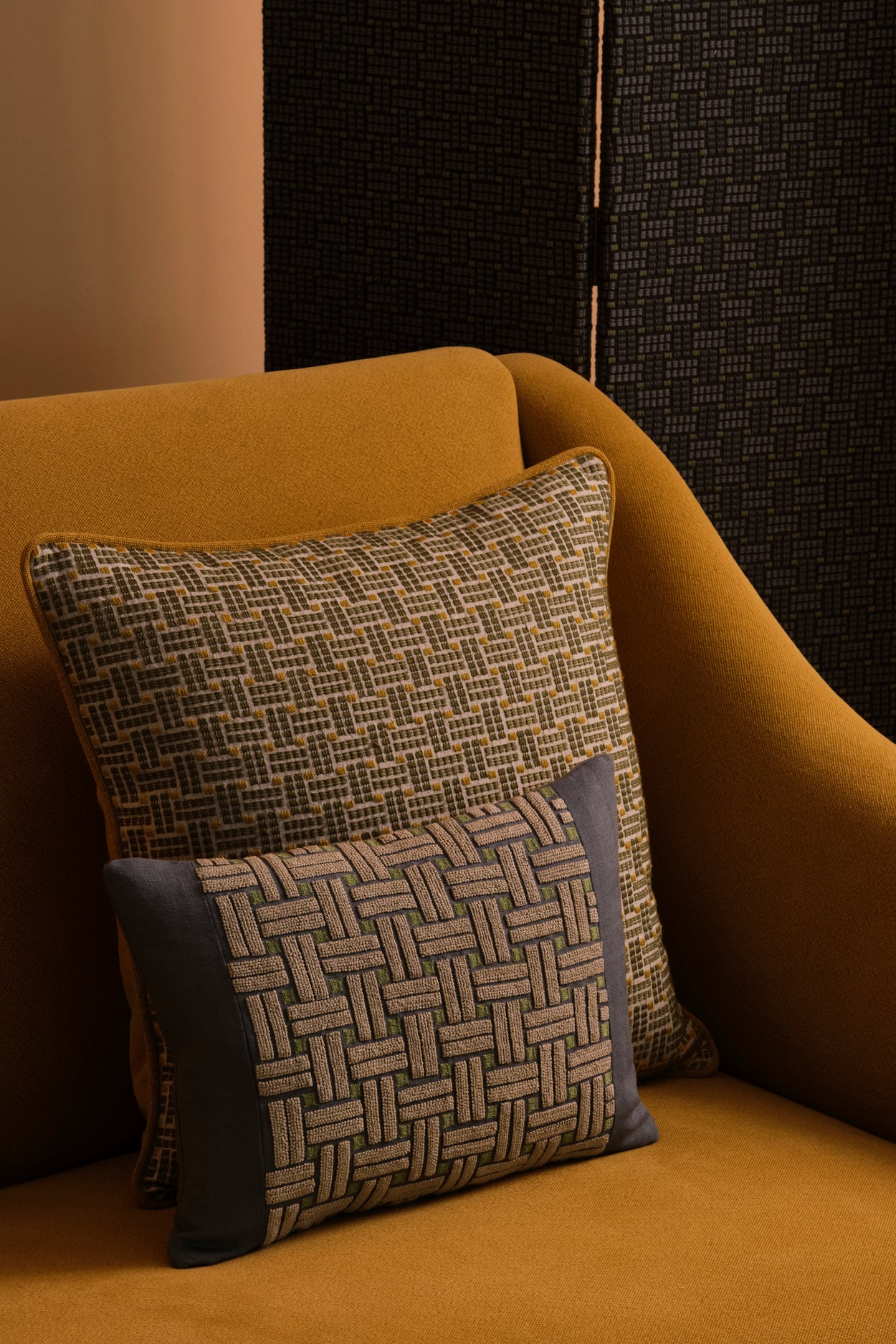 Ochre yellow couch with two embroidered throw pillows in a basketweave design in shades of green, ecru and navy. 