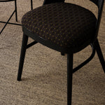 Overhead image of a black lacquer chair with an embroidered seat in a dark blue, along side a metal and rattan side table against a heather grey carpet 