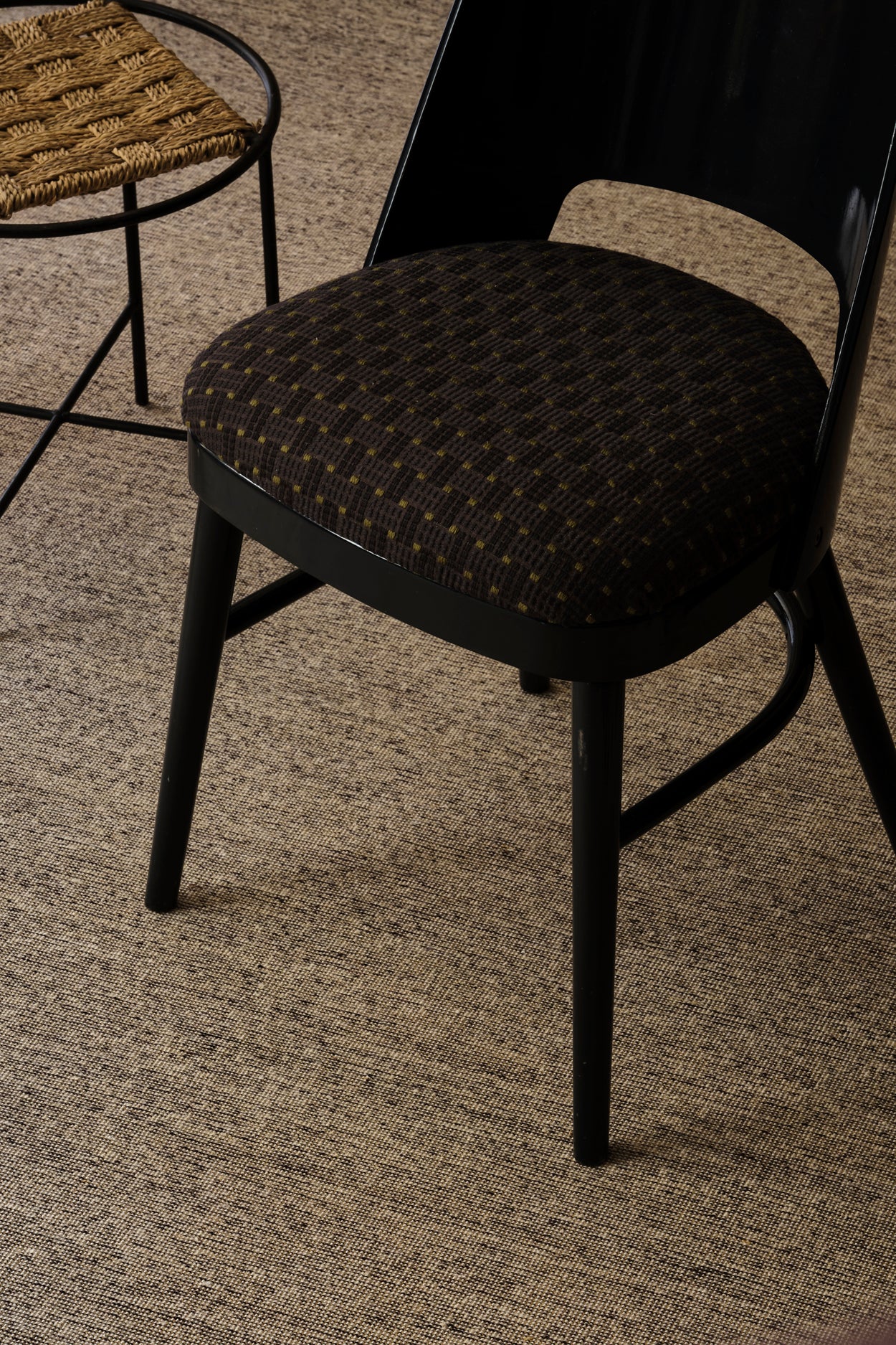 Overhead image of a black lacquer chair with an embroidered seat in a dark blue, along side a metal and rattan side table against a heather grey carpet 