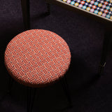 Overhead image of an upholstered stool in a red embroidered fabric with a harlequin enameled side table and stack of books. 