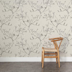 A wooden chair stands in front of a wall papered in a painterly bird and branch pattern in shades of gray on a cream field.