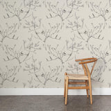 A wooden chair stands in front of a wall papered in a painterly bird and branch pattern in shades of gray on a cream field.