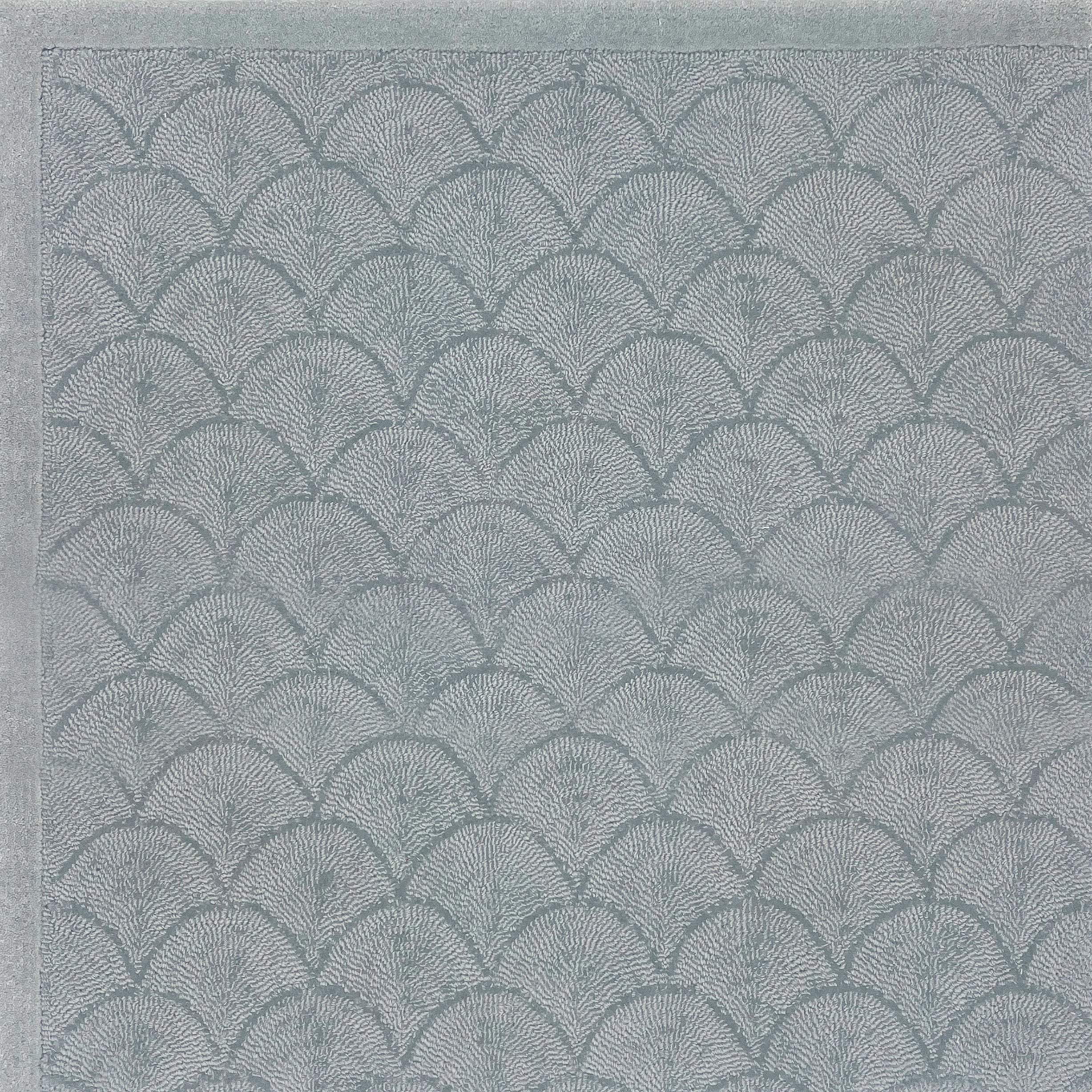 Handtufted rug sample with a repeating scallop pattern in muted blue-gray tones.