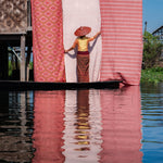 Woman in a boat with a large pink and white striped fabric reflected in water