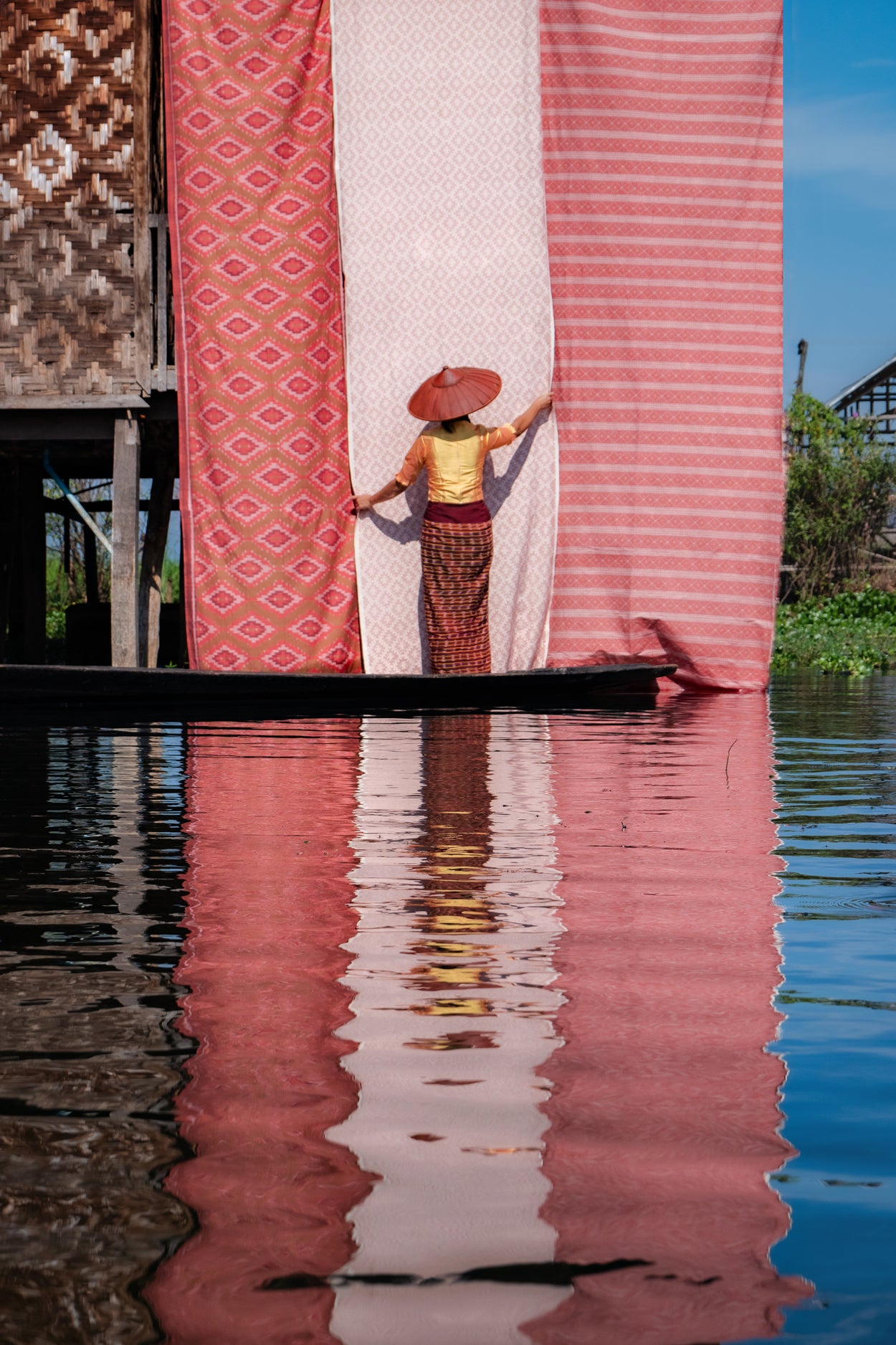 Woman in a boat with a large pink and white striped fabric reflected in water