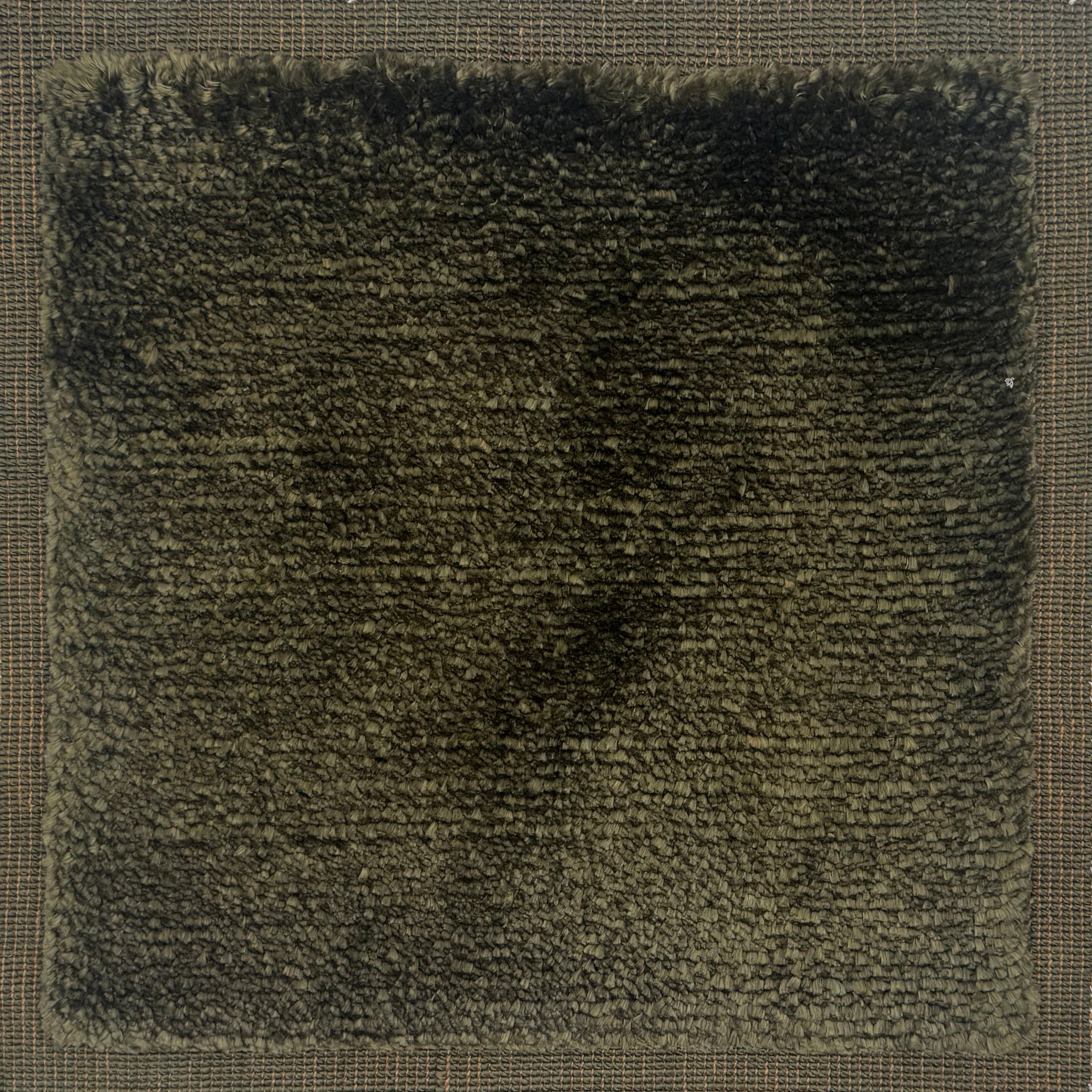 Handloomed rug with tonal border and raised cut pile shag field in dark green.