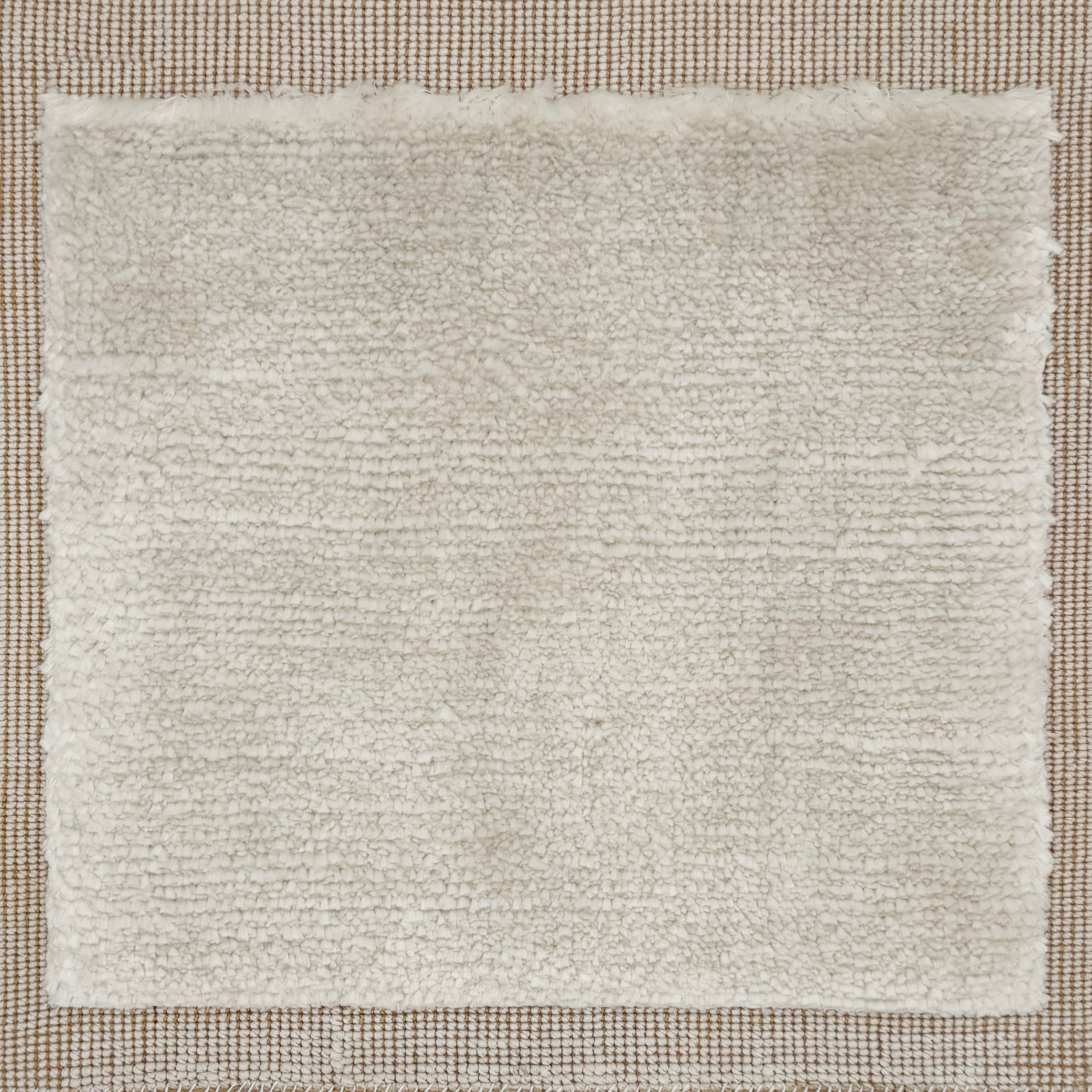 Handloomed rug with neutral border and raised cut pile shag field in cream.