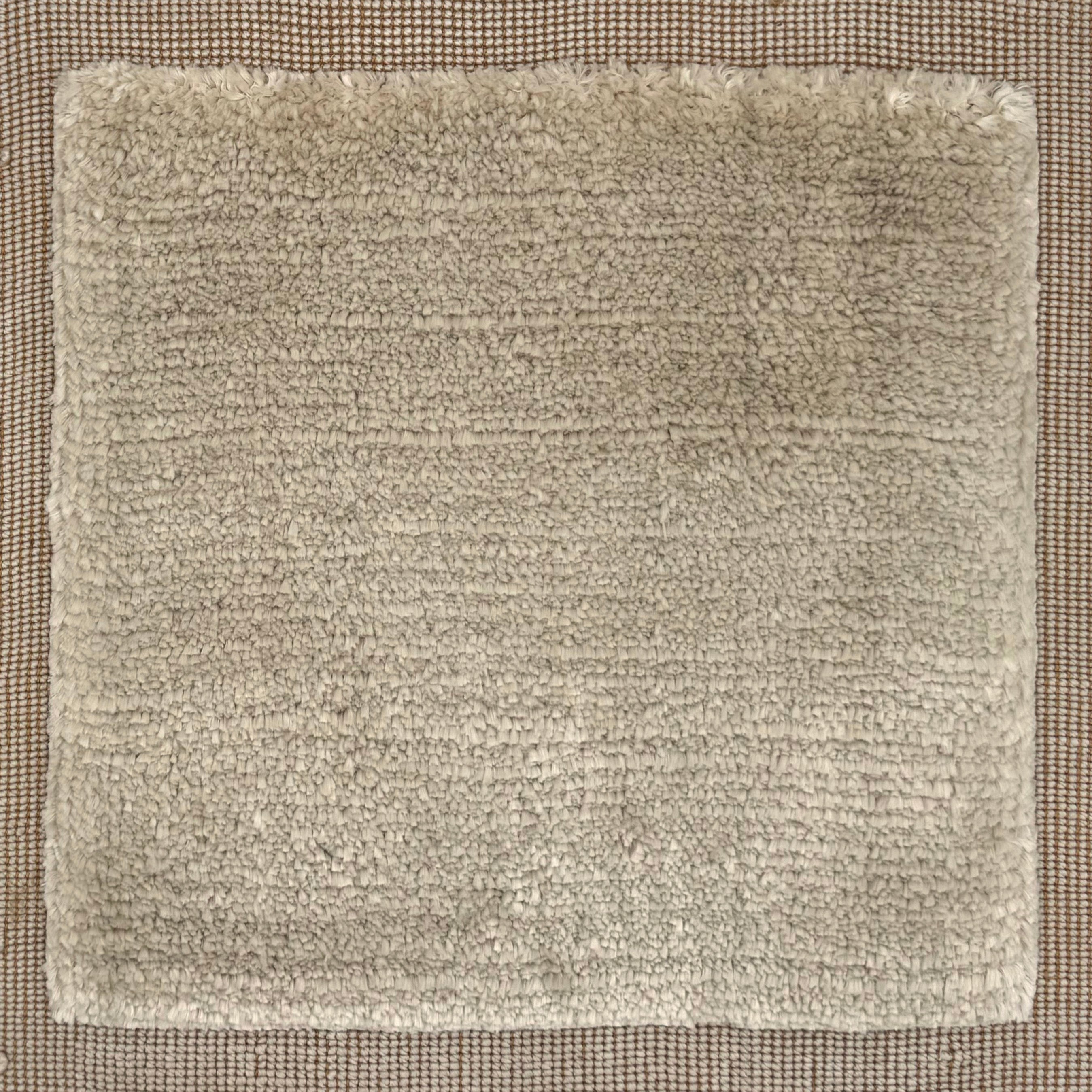 Handloomed rug with neutral border and raised cut pile shag field in taupe. 