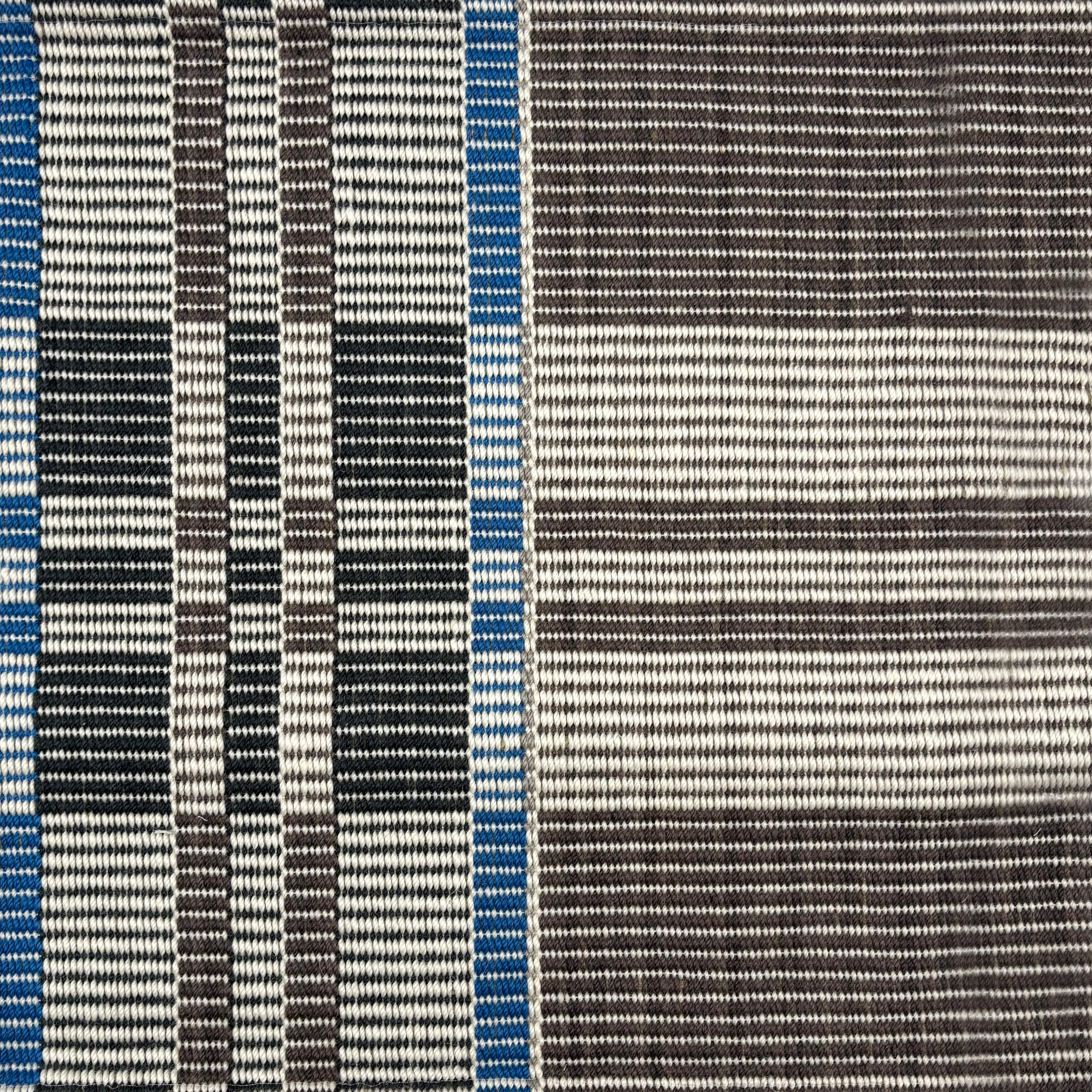 Handwoven rug in a large scale plaid in shades of brown, cream, black and blue. 