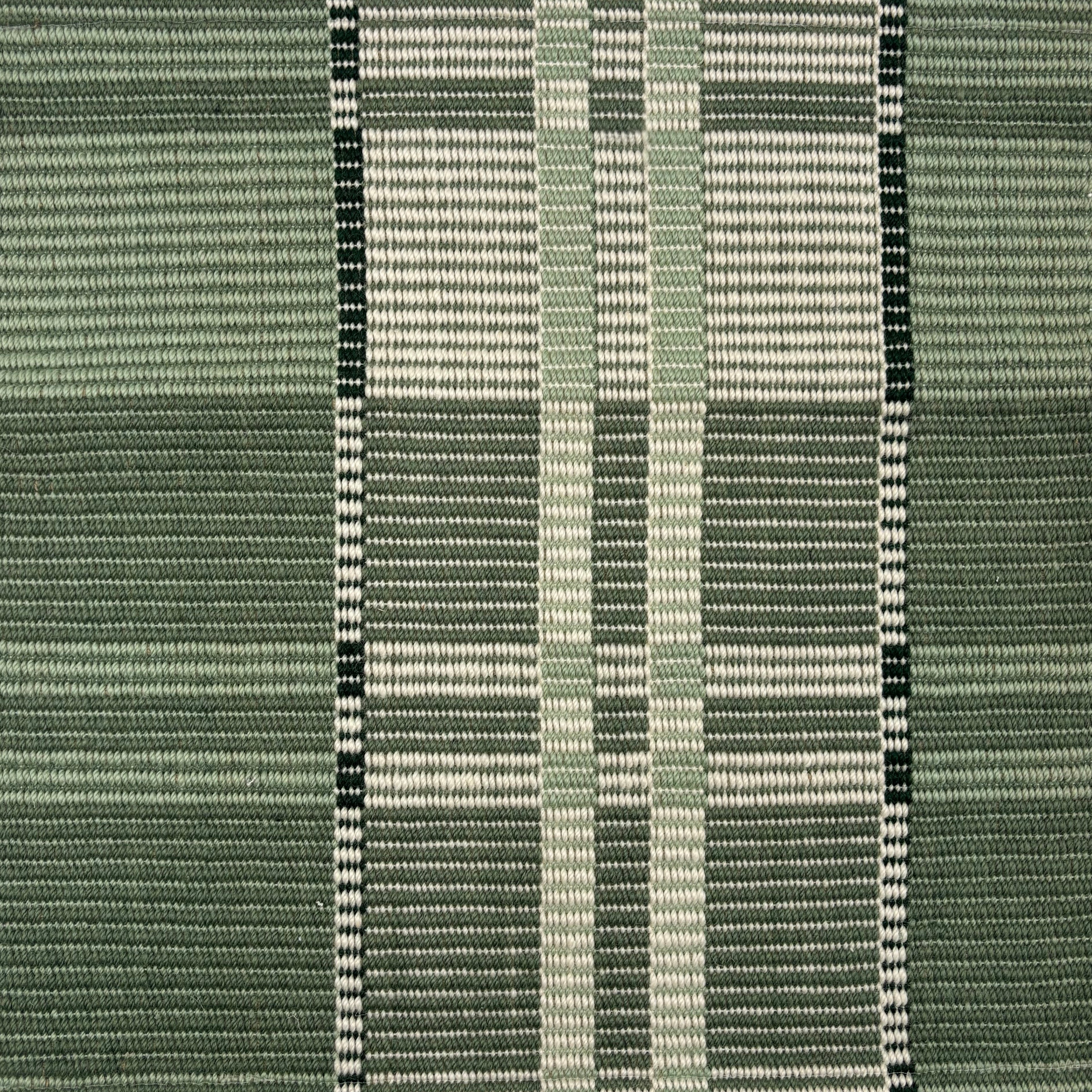 Handwoven rug in a large scale plaid in shades of green and white. 