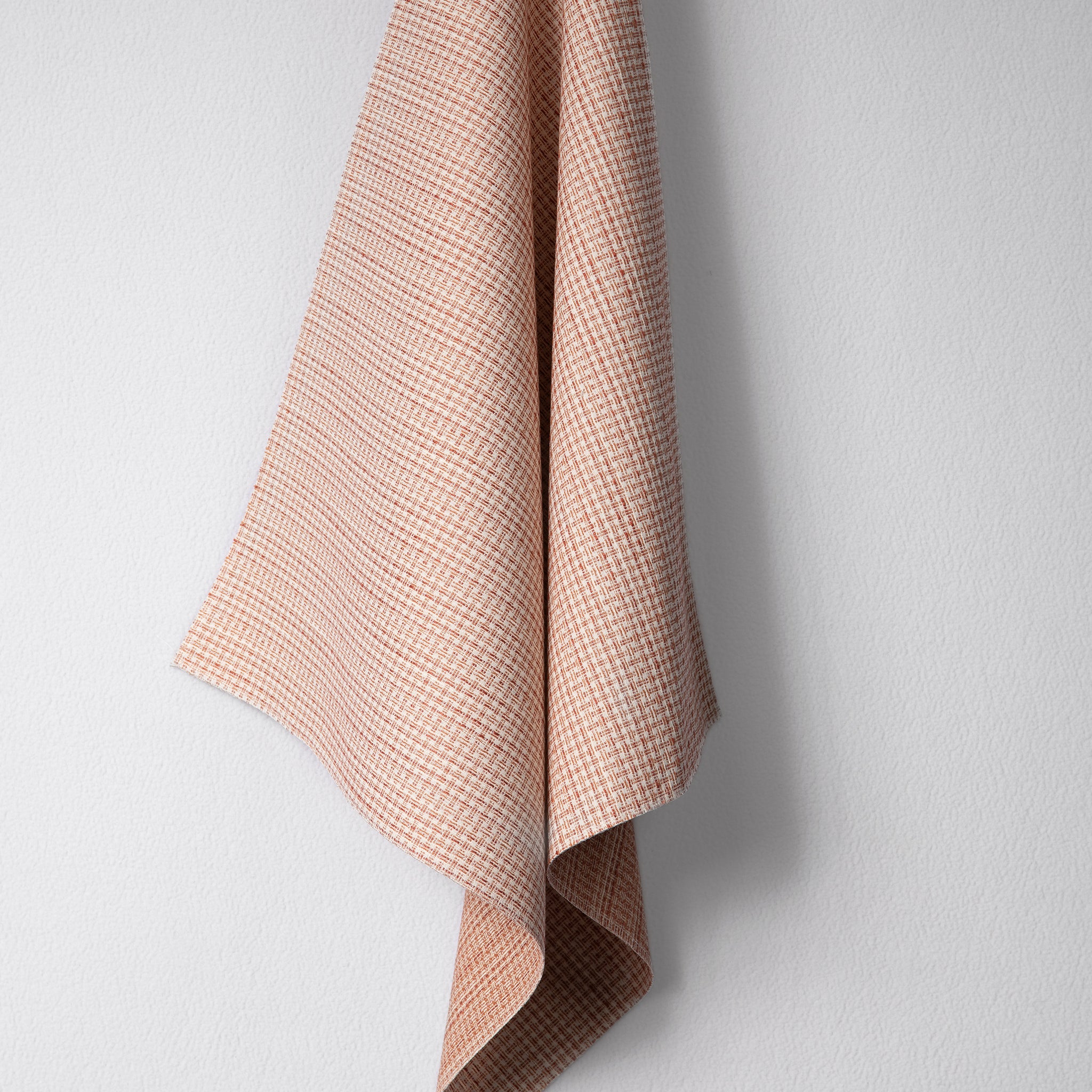 Draped woven outdoor fabric in a subtle check design in orange on a white wall. 