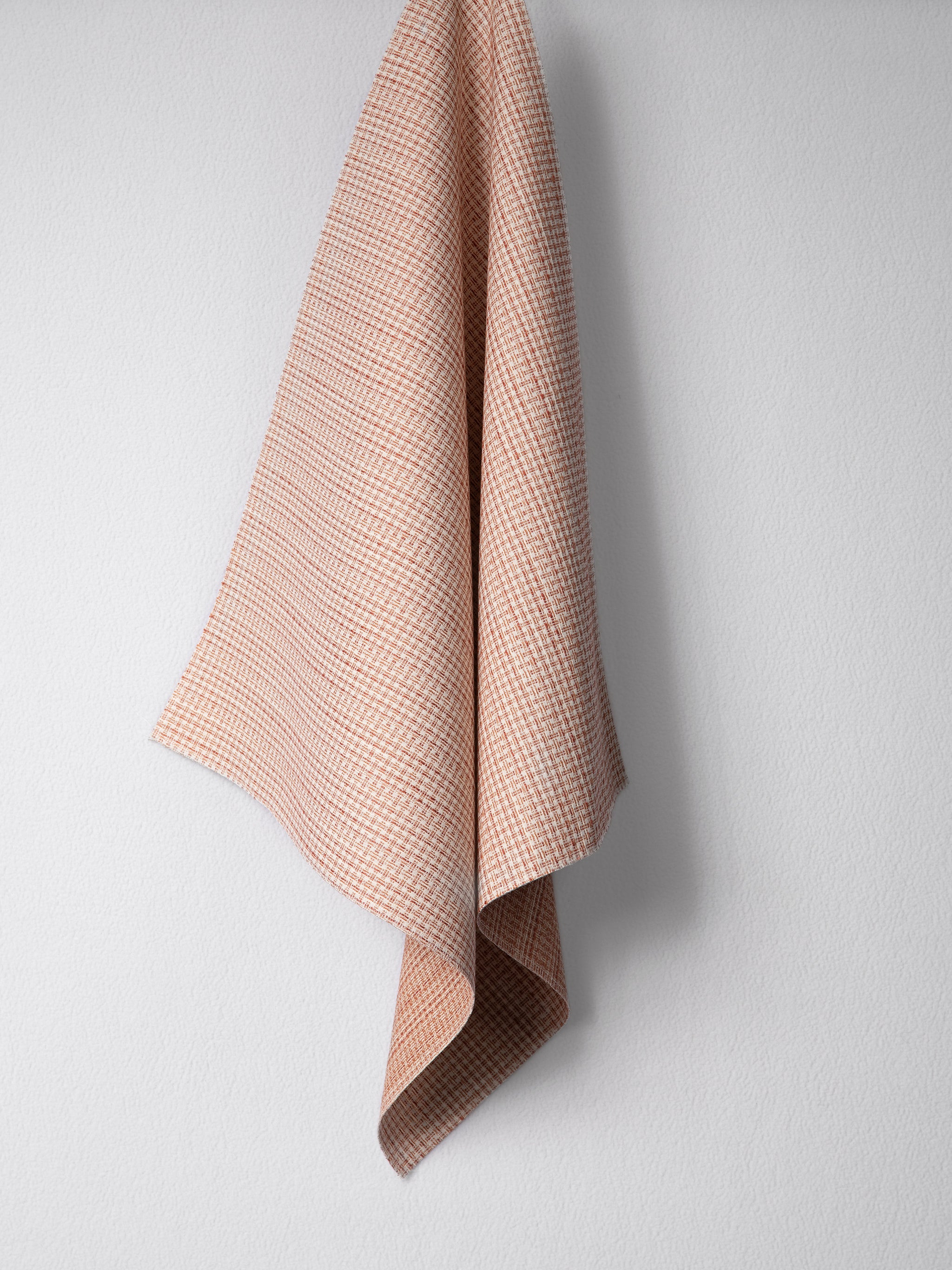 Draped woven outdoor fabric in a subtle check design in orange on a white wall. 