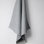 Draped woven outdoor fabric in a subtle check design in blue on a white wall. 