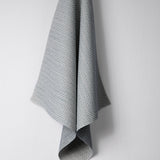 Draped woven outdoor fabric in a subtle check design in blue on a white wall. 