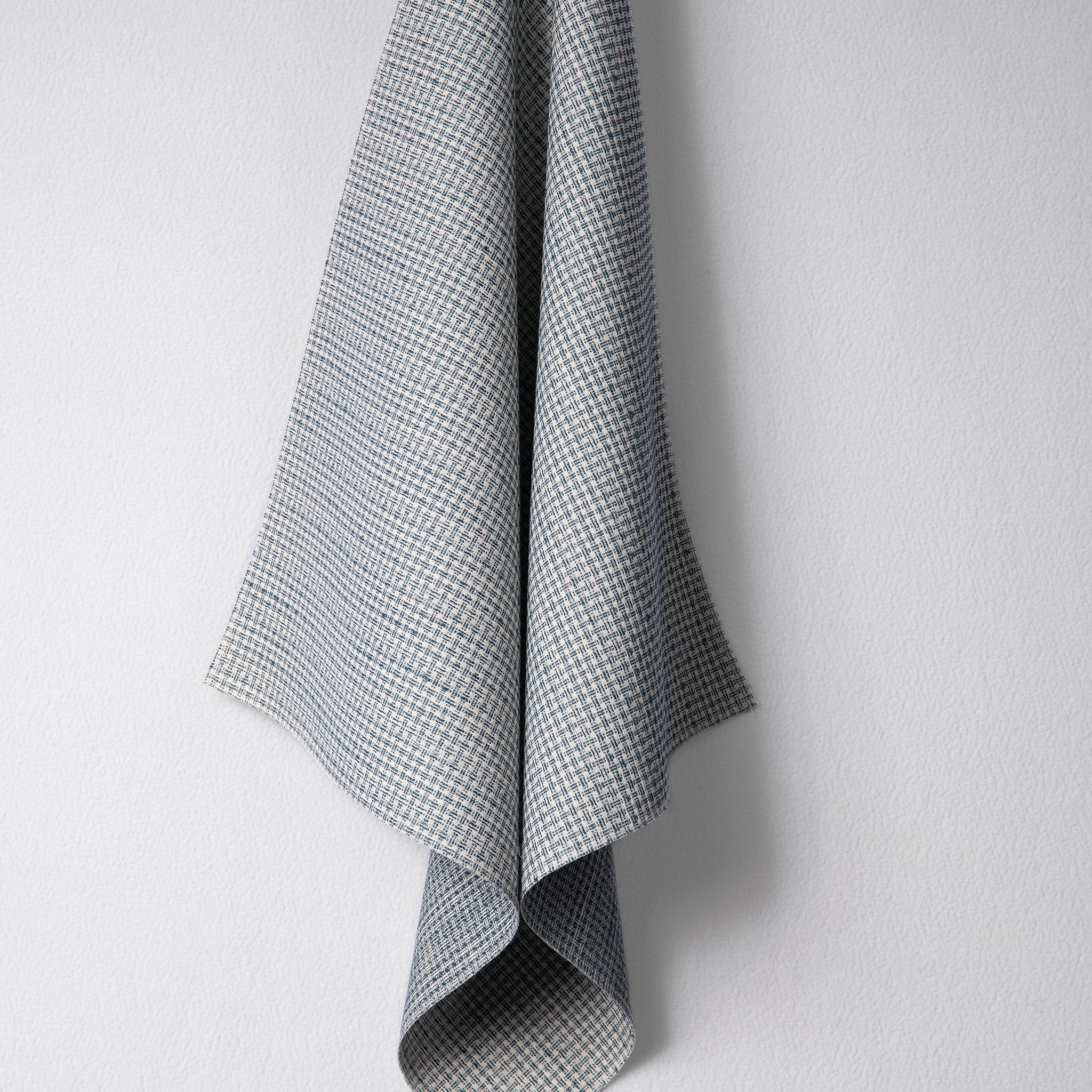 Draped woven outdoor fabric in a subtle check design in blue on a white wall. 