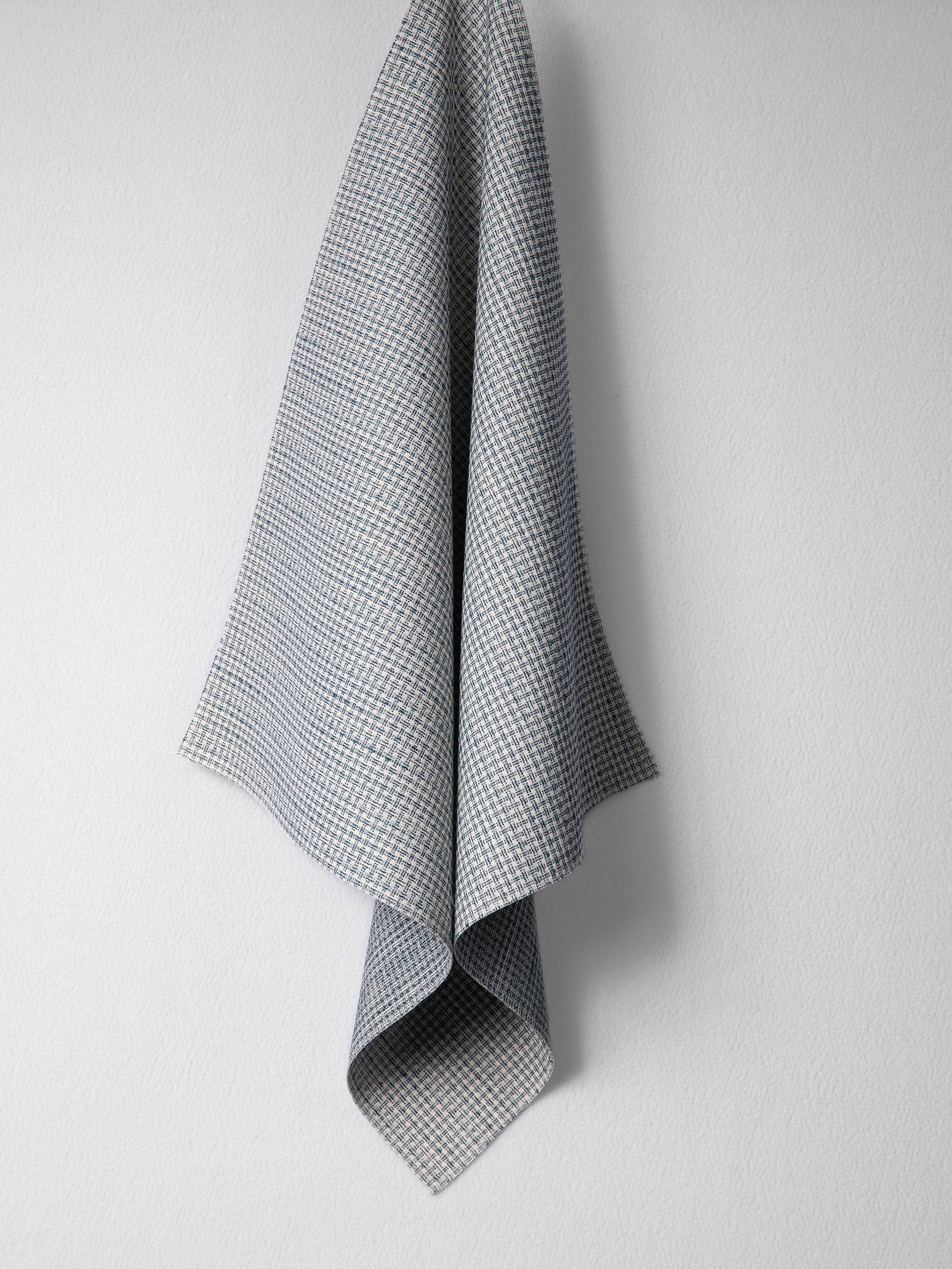Draped woven outdoor fabric in a subtle check design in blue on a white wall. 