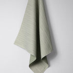 Draped woven outdoor fabric in a subtle check design in green on a white wall. 