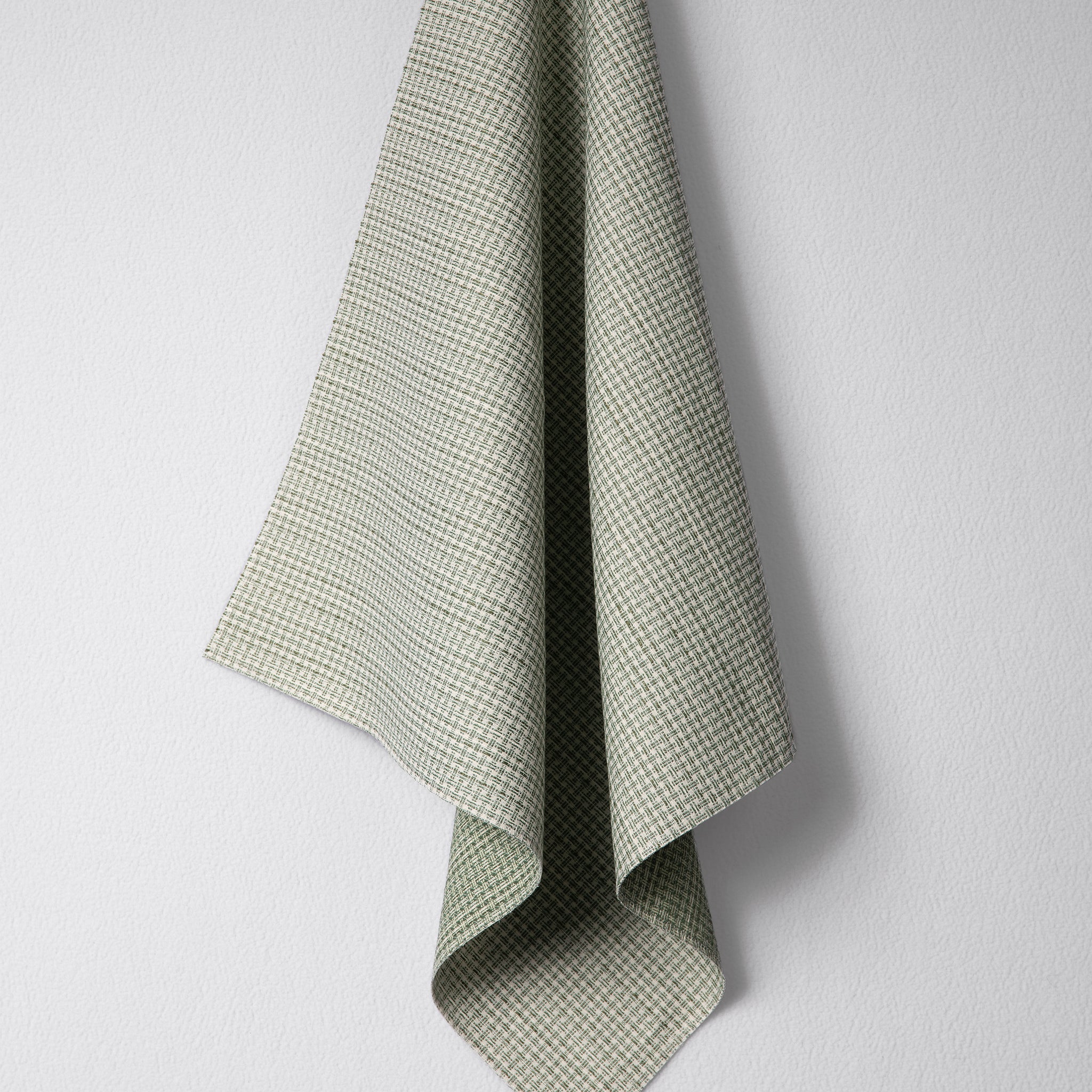 Draped woven outdoor fabric in a subtle check design in green on a white wall. 
