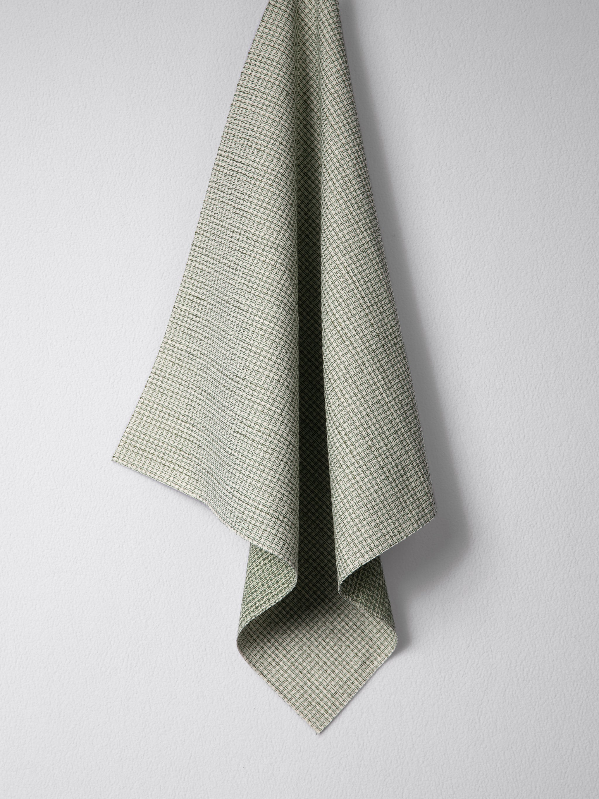 Draped woven outdoor fabric in a subtle check design in green on a white wall. 
