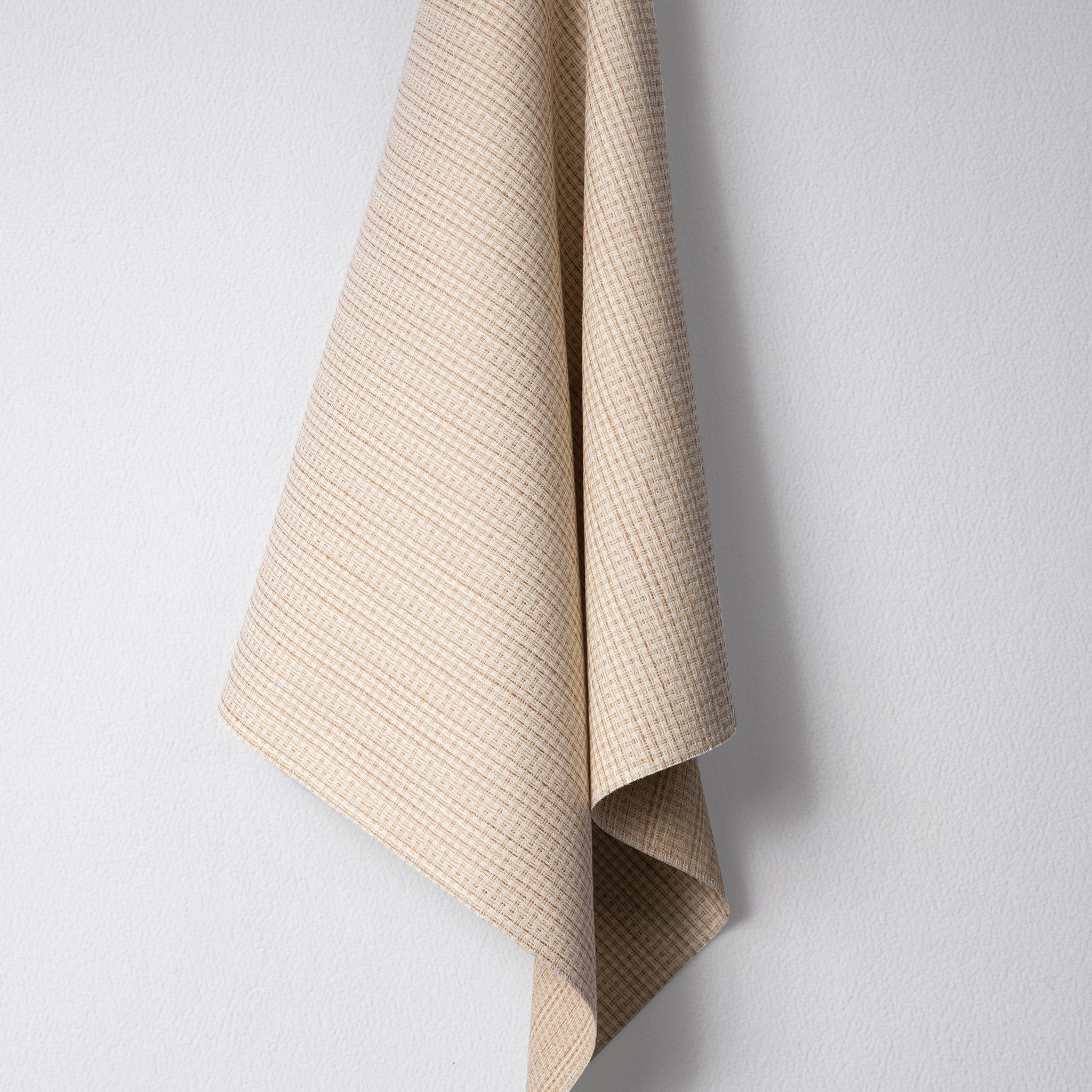 Draped woven outdoor fabric in a subtle check design in tan on a white wall. 