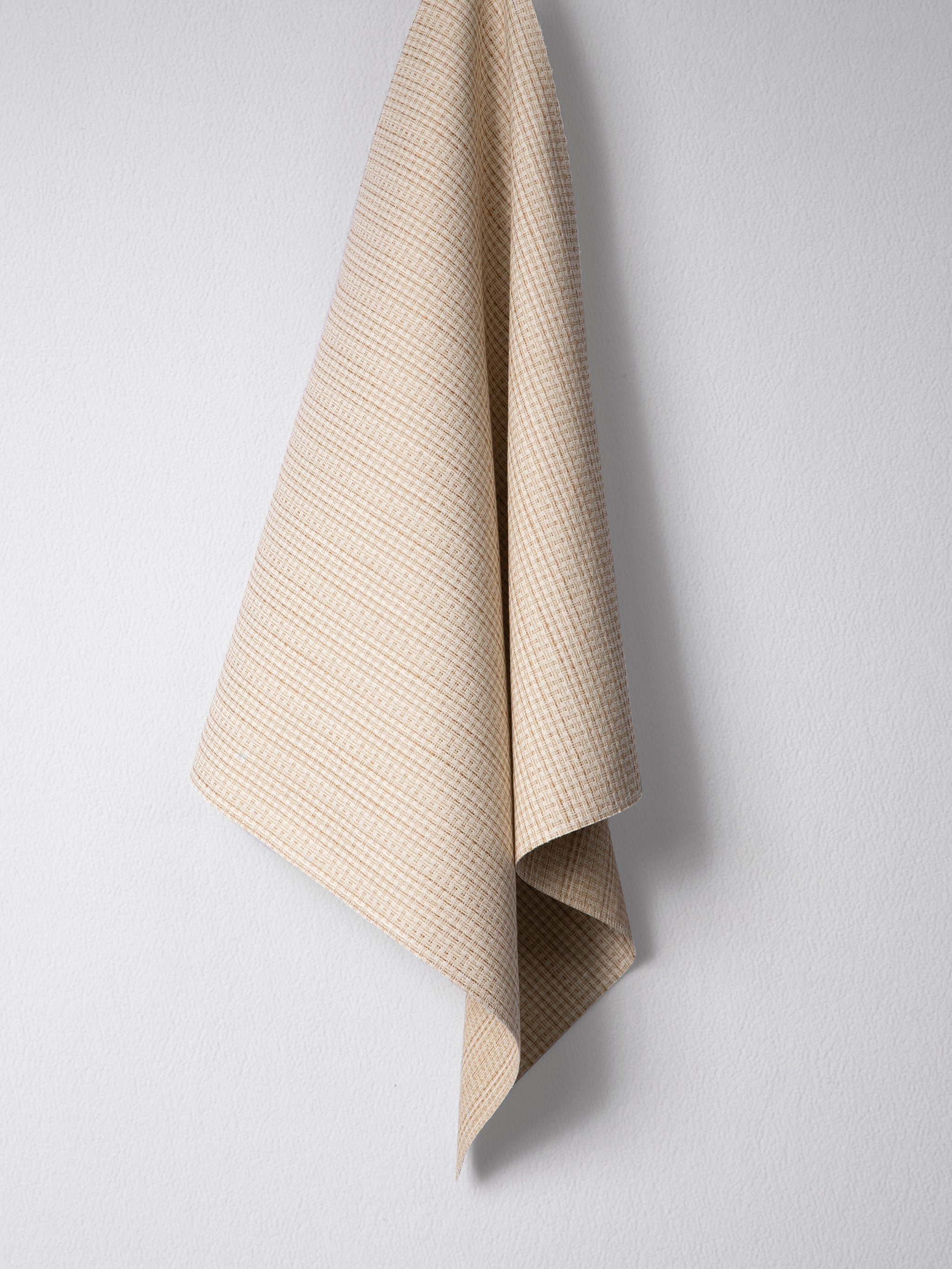 Draped woven outdoor fabric in a subtle check design in tan on a white wall. 