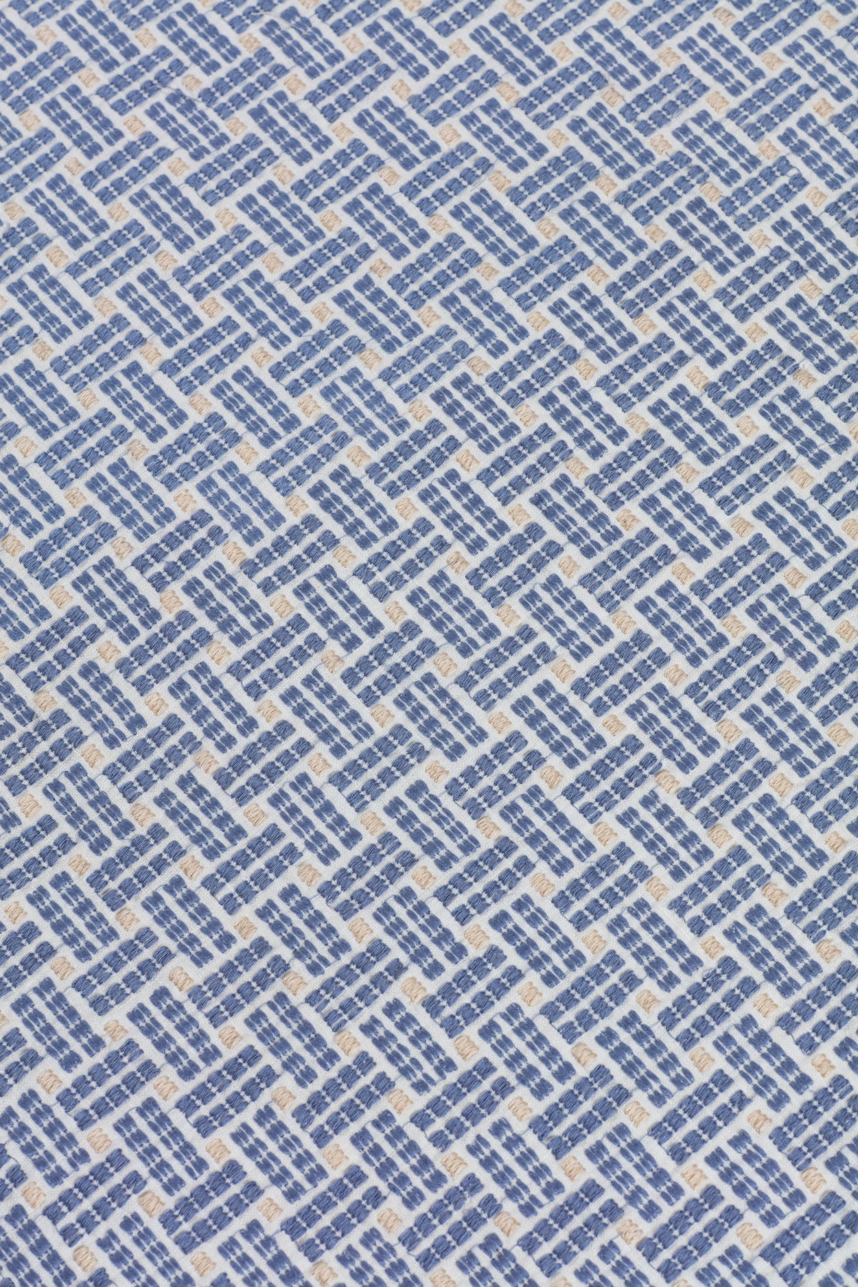 Close up of embroidered fabric with a basketweave design in blue on a white field. 