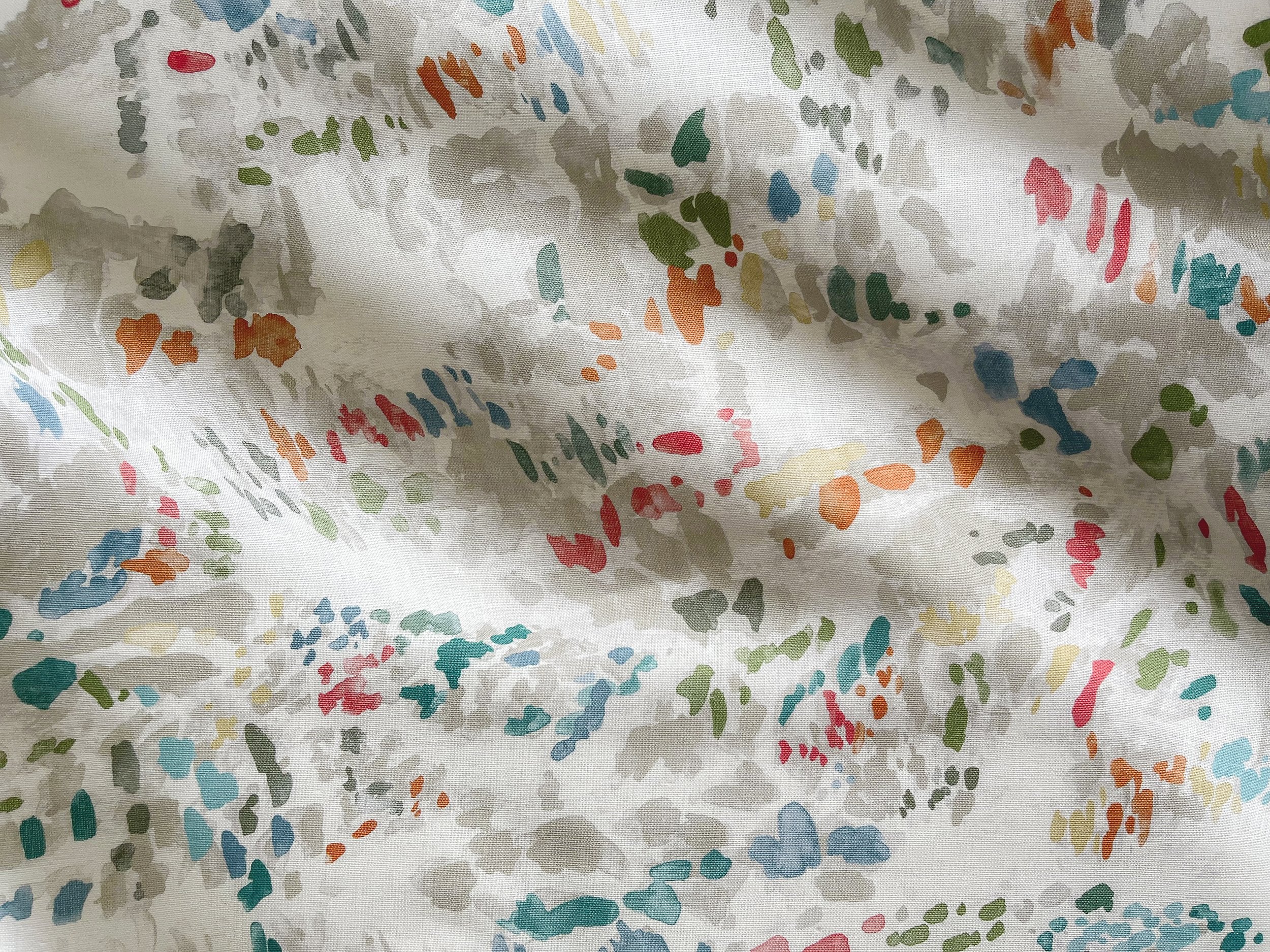 Draped fabric yardage in a painterly cloud print in shades of red, green, tan and blue on a cream field.